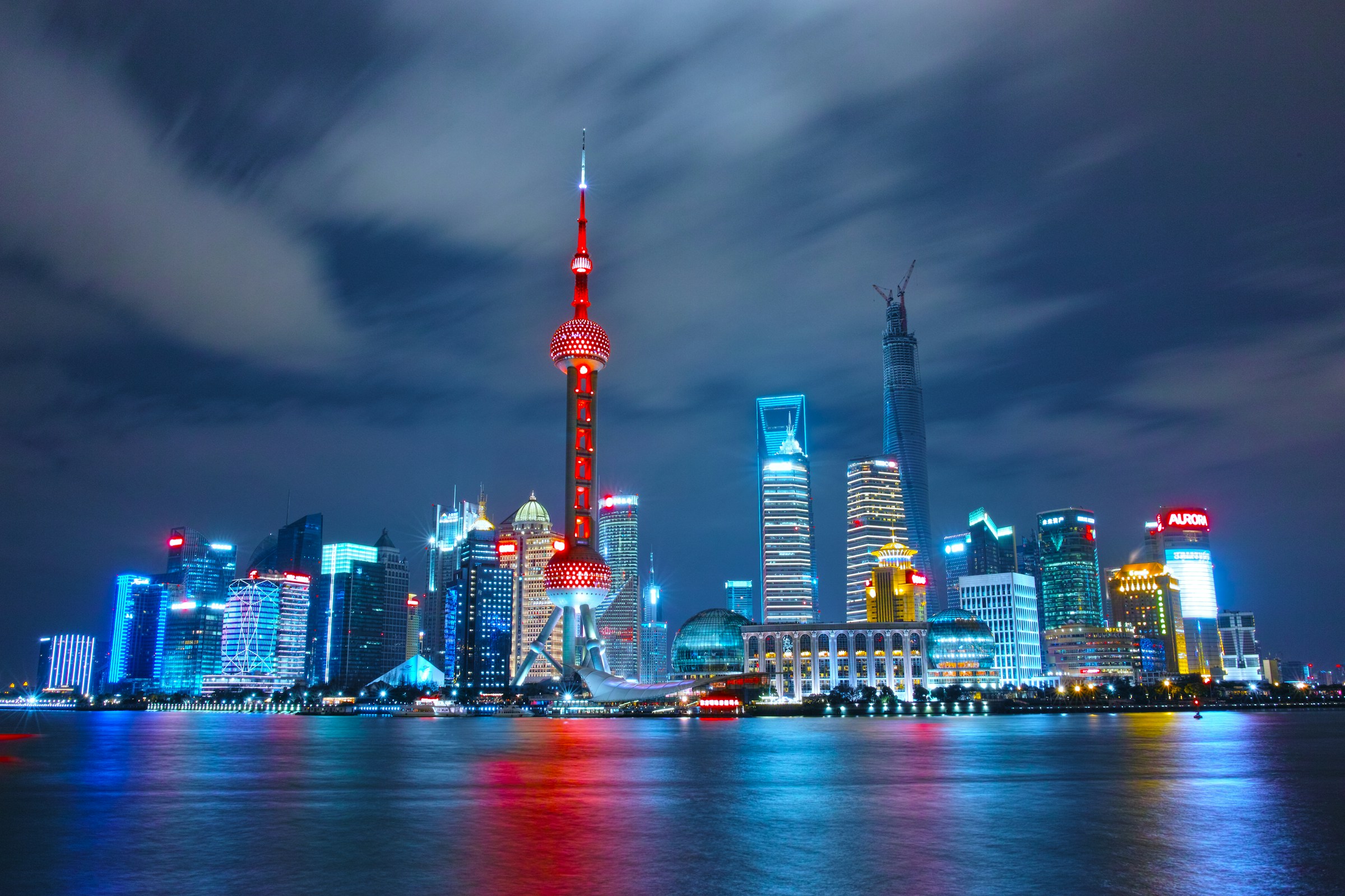Shanghai skyline at night featuring illuminated modern skyscrapers, including the Oriental Pearl Tower, reflecting on the Huangpu River
