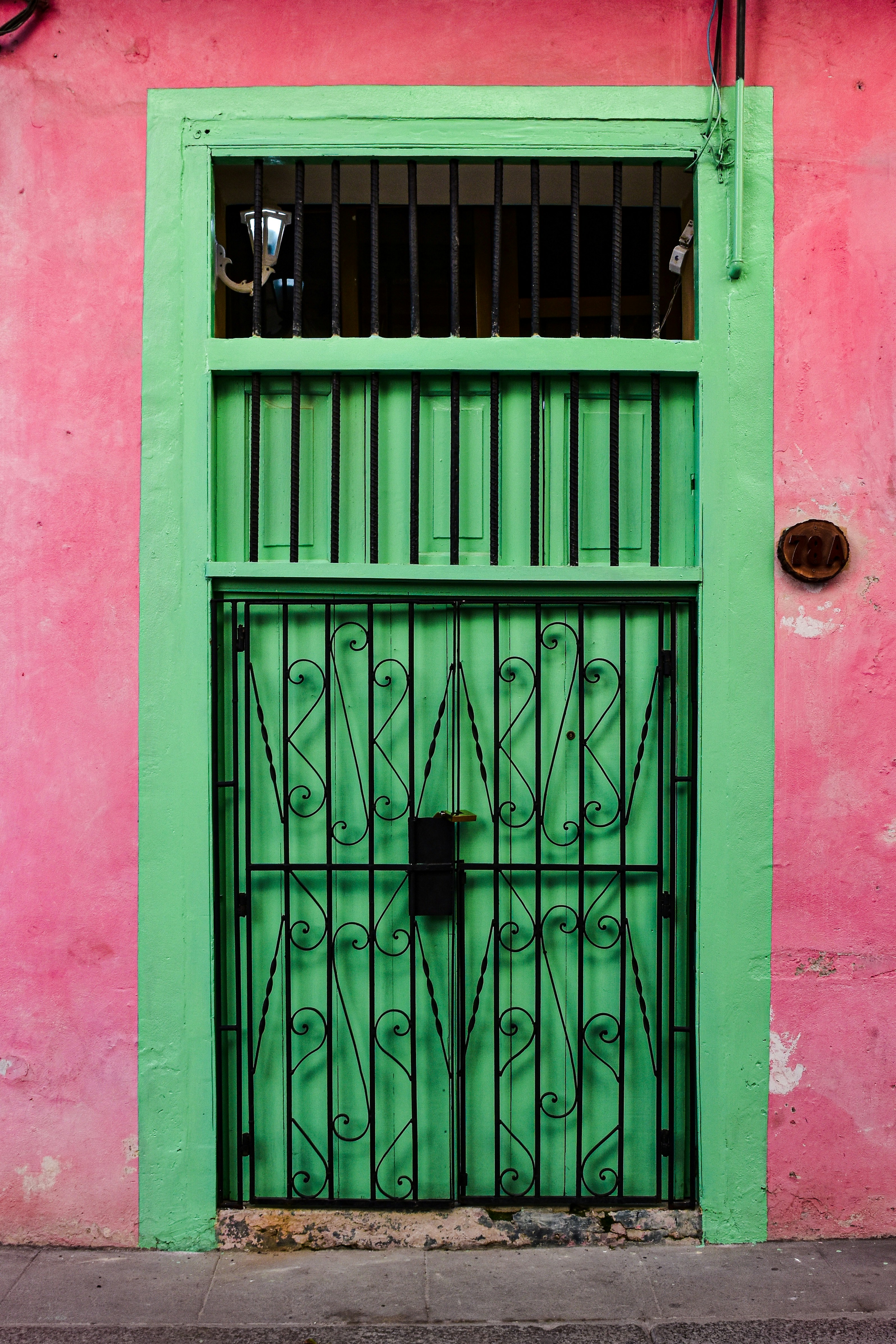 Livlig grøn metaldør med dekorativt sort jernrist, sat op mod en farverig lyserød væg