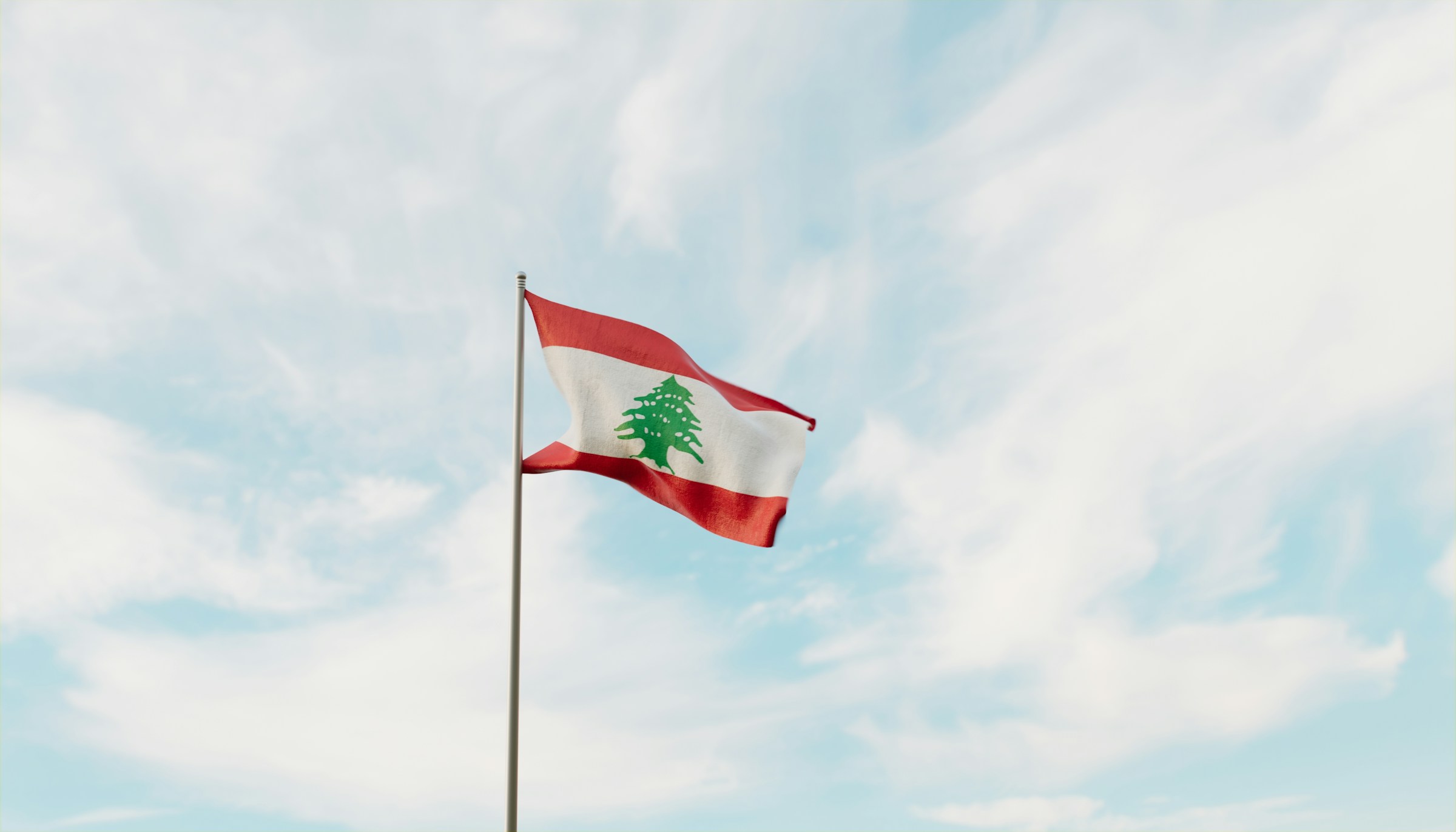 Lebanese flag waving against a partly cloudy blue sky