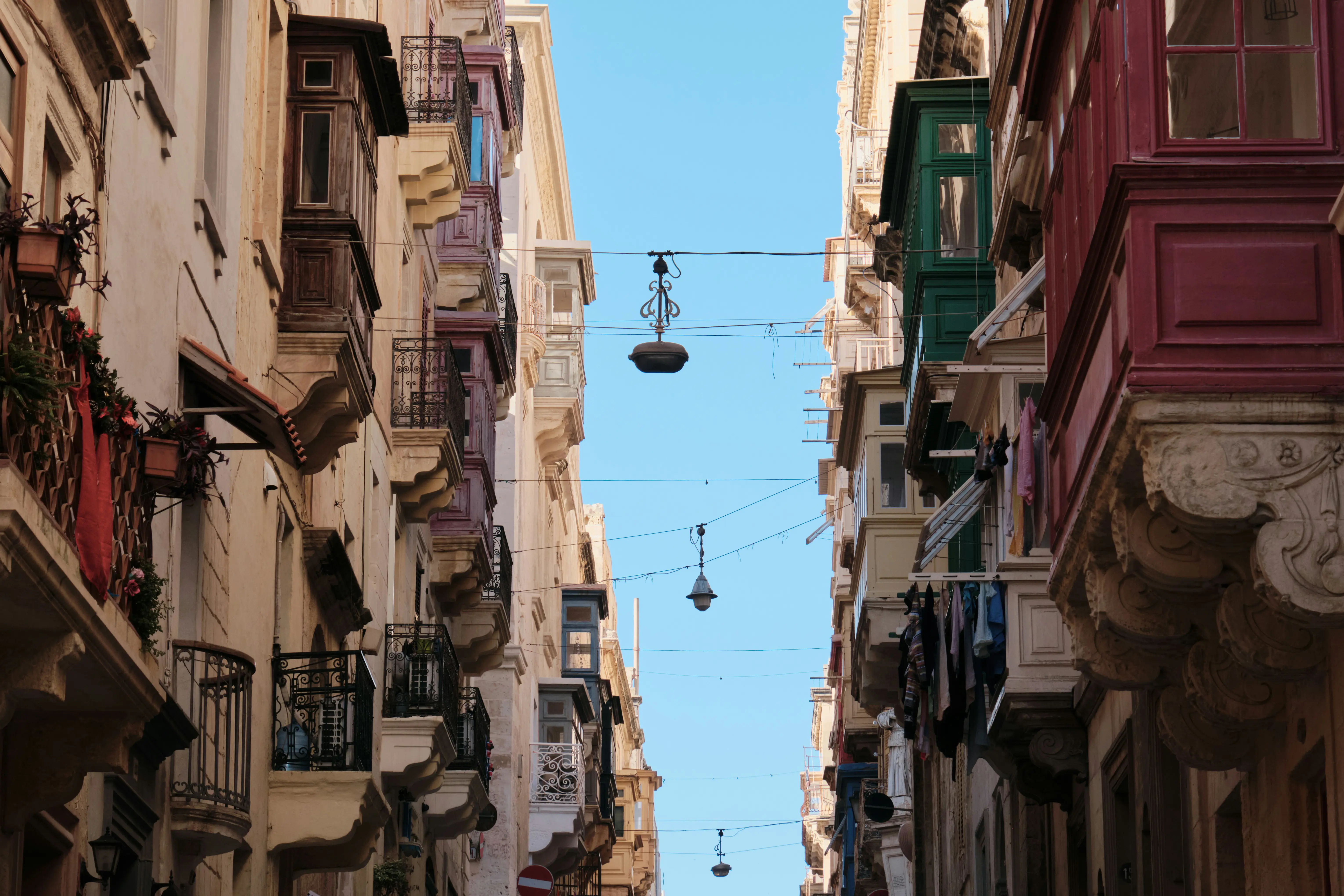 Smal gade med traditionelle maltesiske altaner under en klar blå himmel i Valletta, Malta