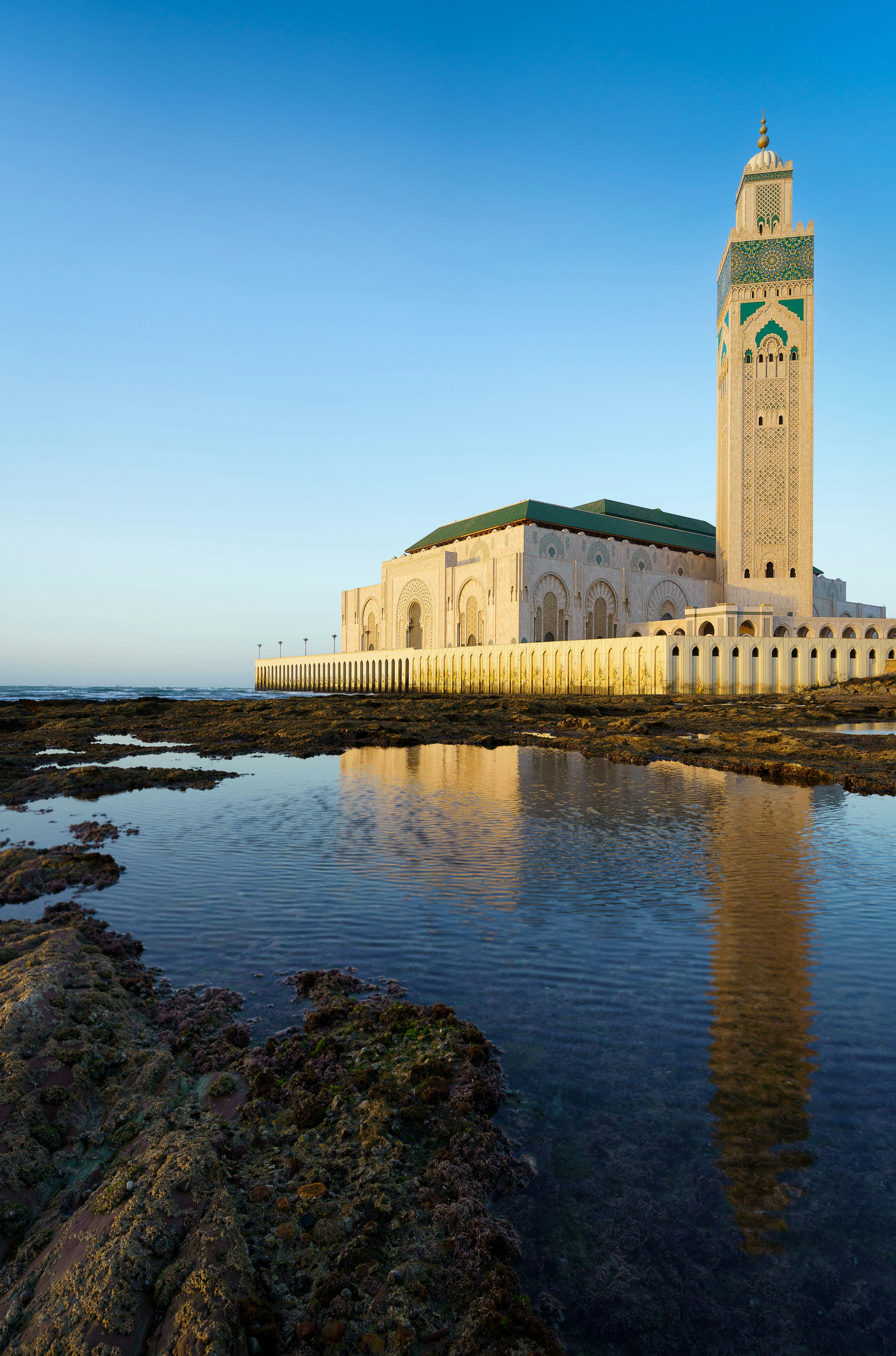 Hassan II-moskeen i Casablanca, Marokko, spejlet i rolige kystvande under en klar blå himmel