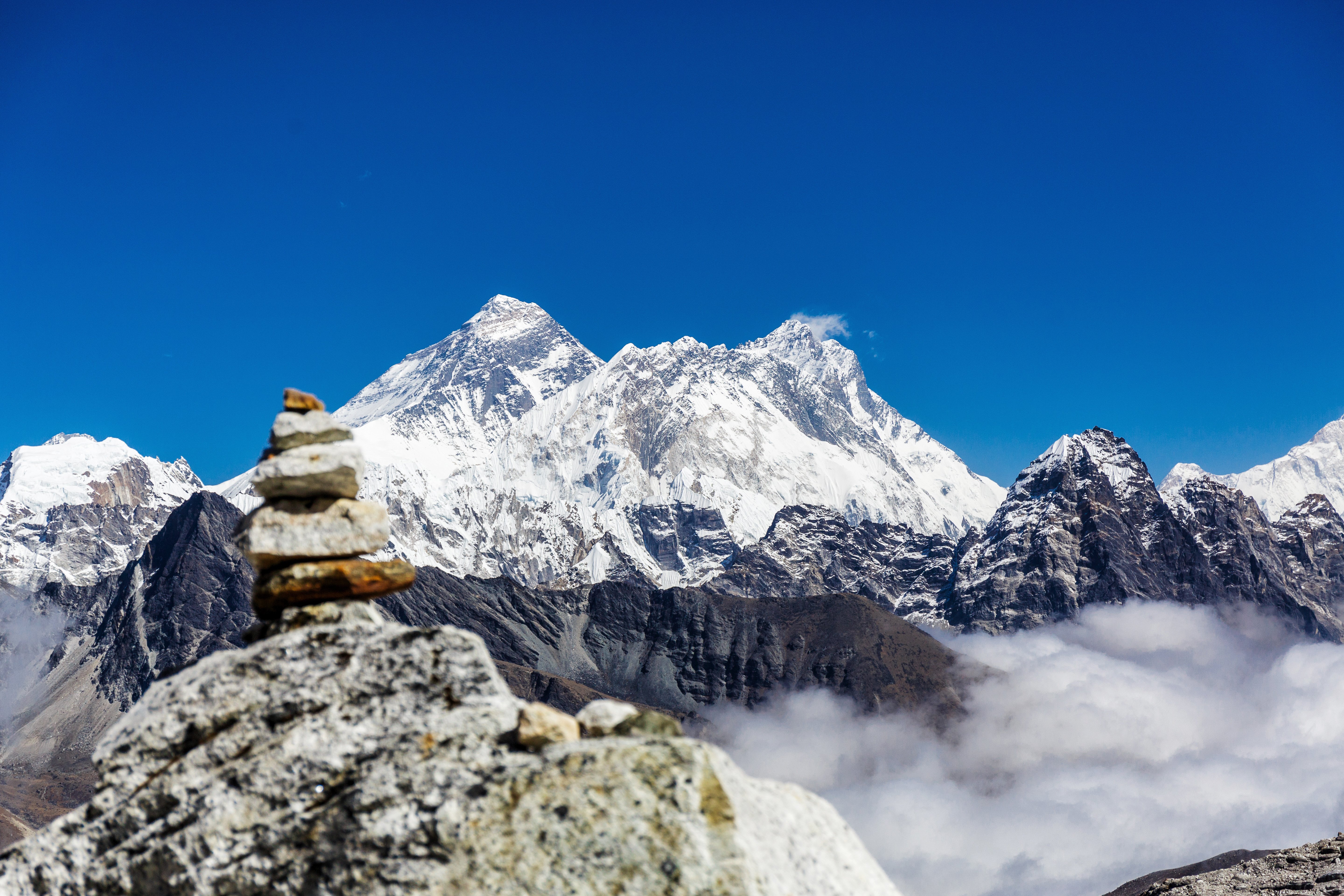 Stablerede sten i forgrunden med Mount Everest og Himalaya-bjergkæden under en klar blå himmel i baggrunden