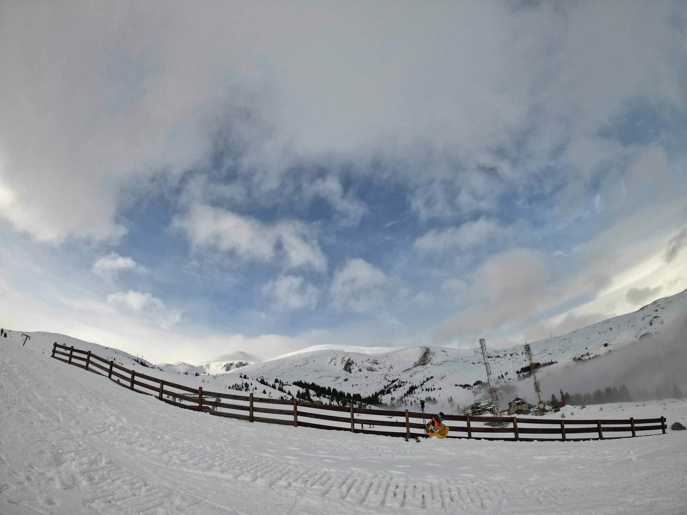 En snedækket skibakke med en delvist skyet himmel og bjerge i baggrunden