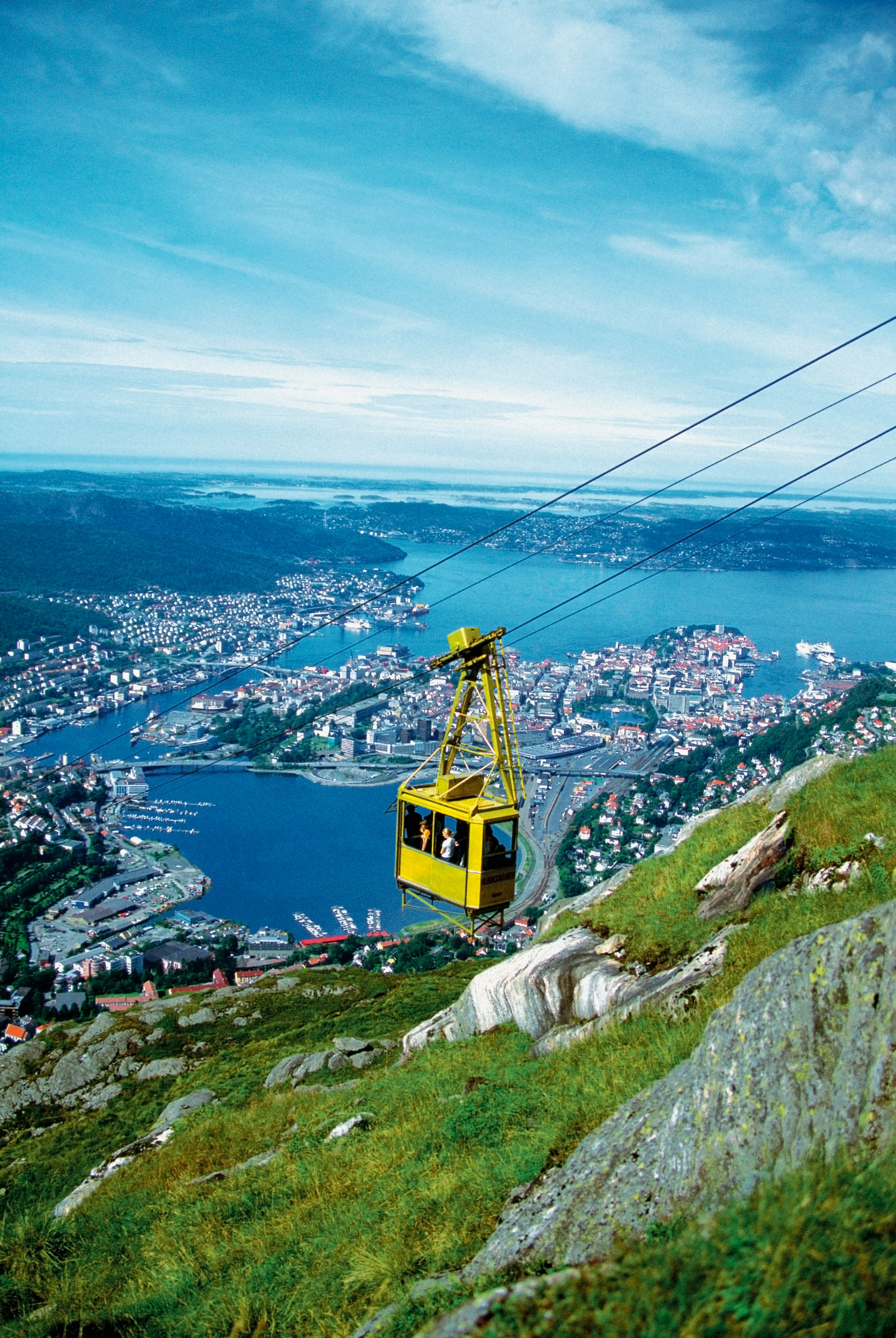 Gul kabelbane opstiger Mount Fløyen med panoramisk udsigt over Bergen, Norge, inklusive bylandskab og havn under en klar blå himmel
