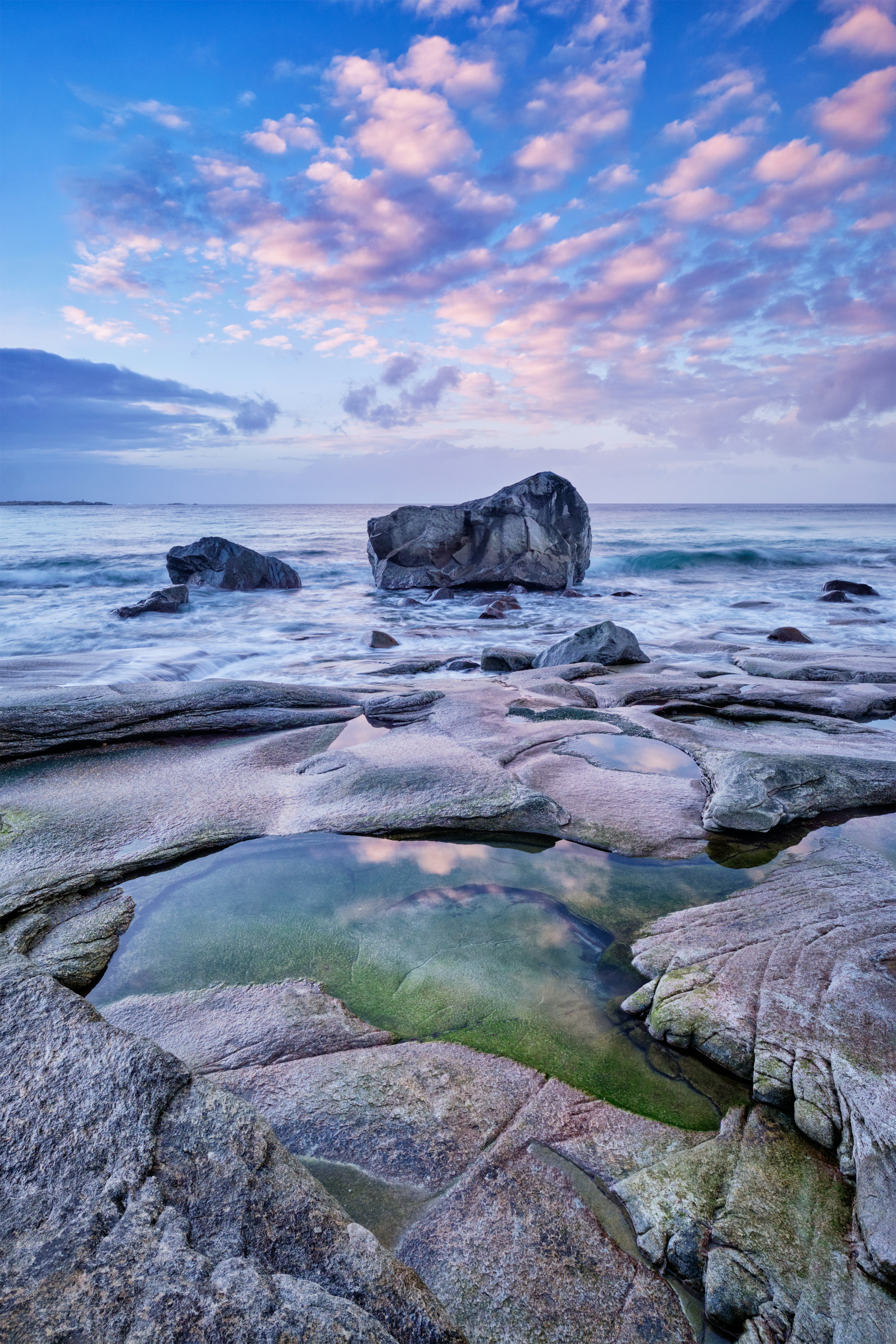 Klippelandskab ved kysten med havudsigt, pink skyer og reflekterende vandpøl i forgrunden