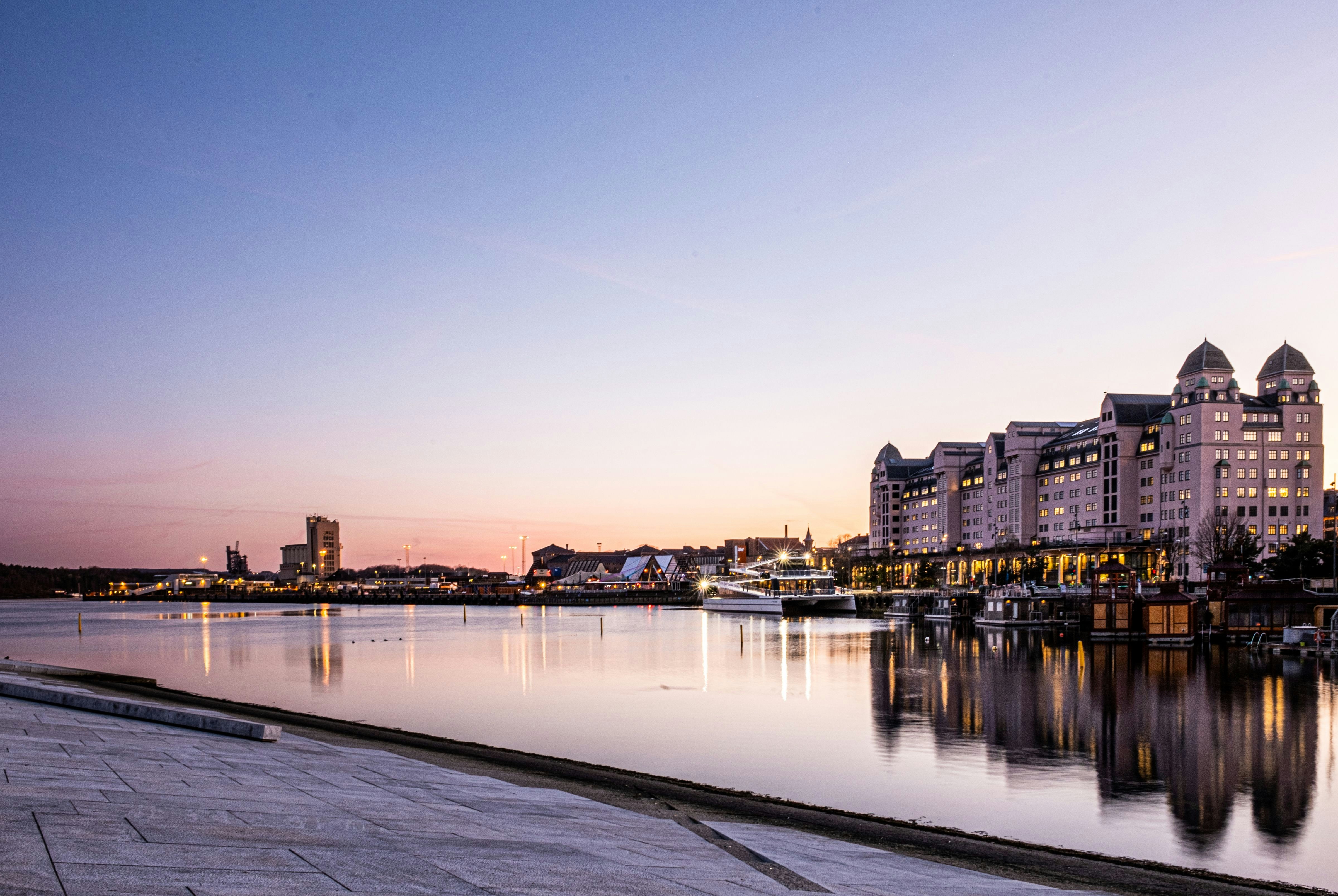 Waterfront view of Oslo, Norway at sunset with modern buildings reflecting in the calm harbor waters, capturing the city's serene evening ambiance