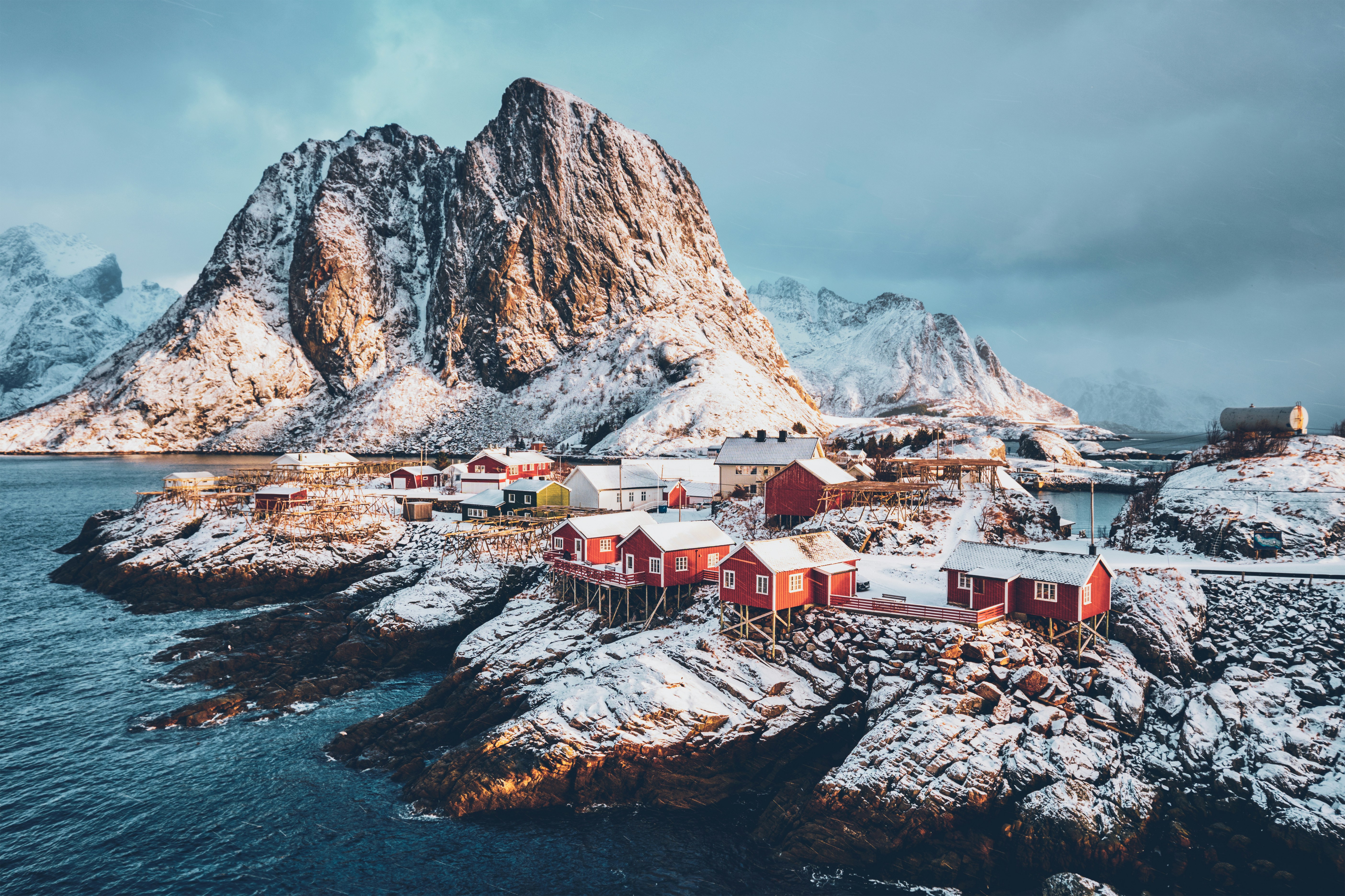 Scenic view of a snowy coastal village with red houses and mountainous backdrop in Lofoten, Norway