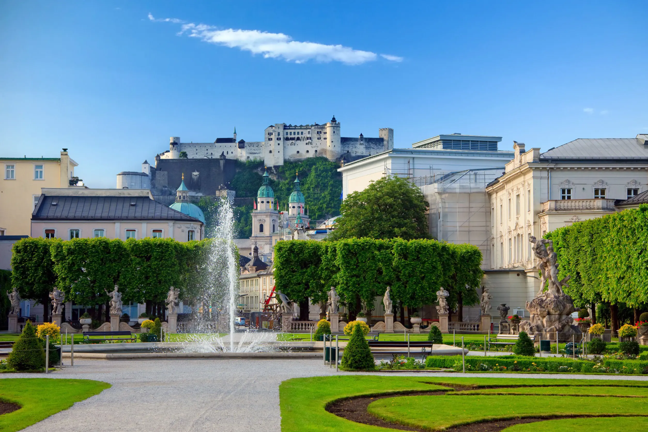 Smuk grøn park med traditionelle europæiske bygninger og springvand mod en blå himmel i Salzburg