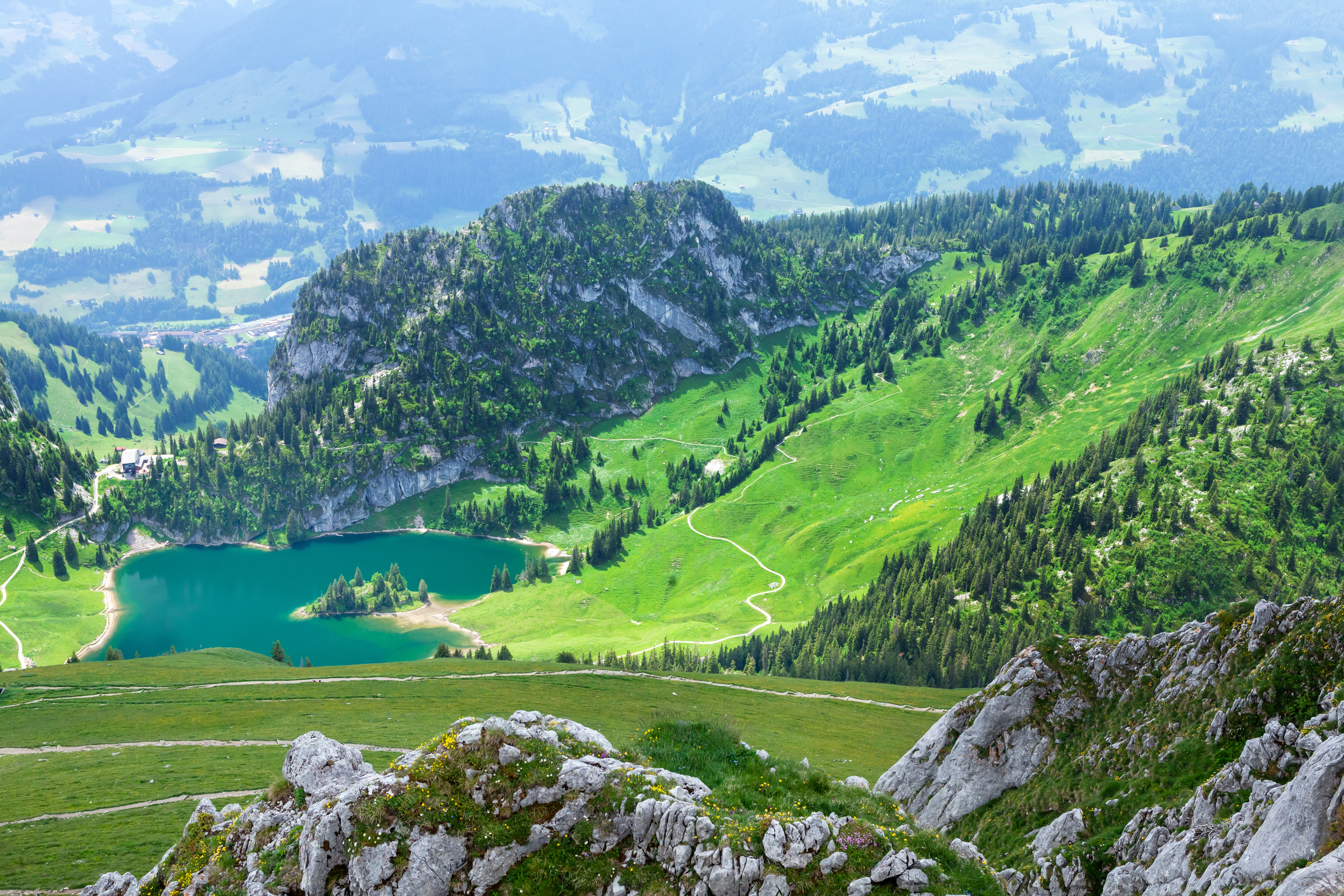 Naturskønt udsyn til frodige grønne bjerge, der omgiver en klar blå alpesø, med klippefyldte skrænter og snoede stier i en fredfyldt, naturlig omgivelser