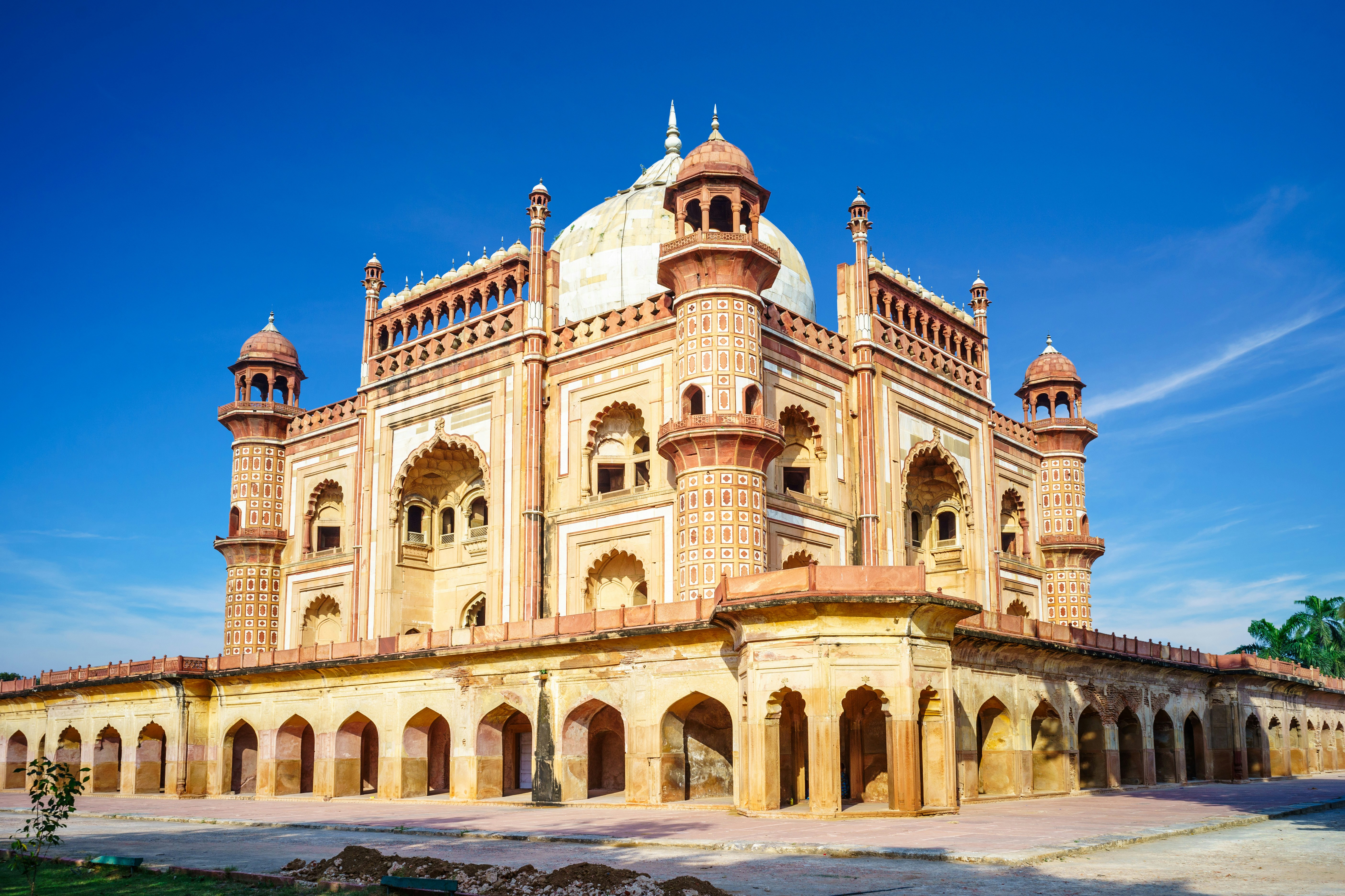 Historisk Mughal-arkitektur af Safdarjung-graven i New Delhi, Indien, med indviklede sandstensudskæringer og kuppelformede tage under en klar blå himmel