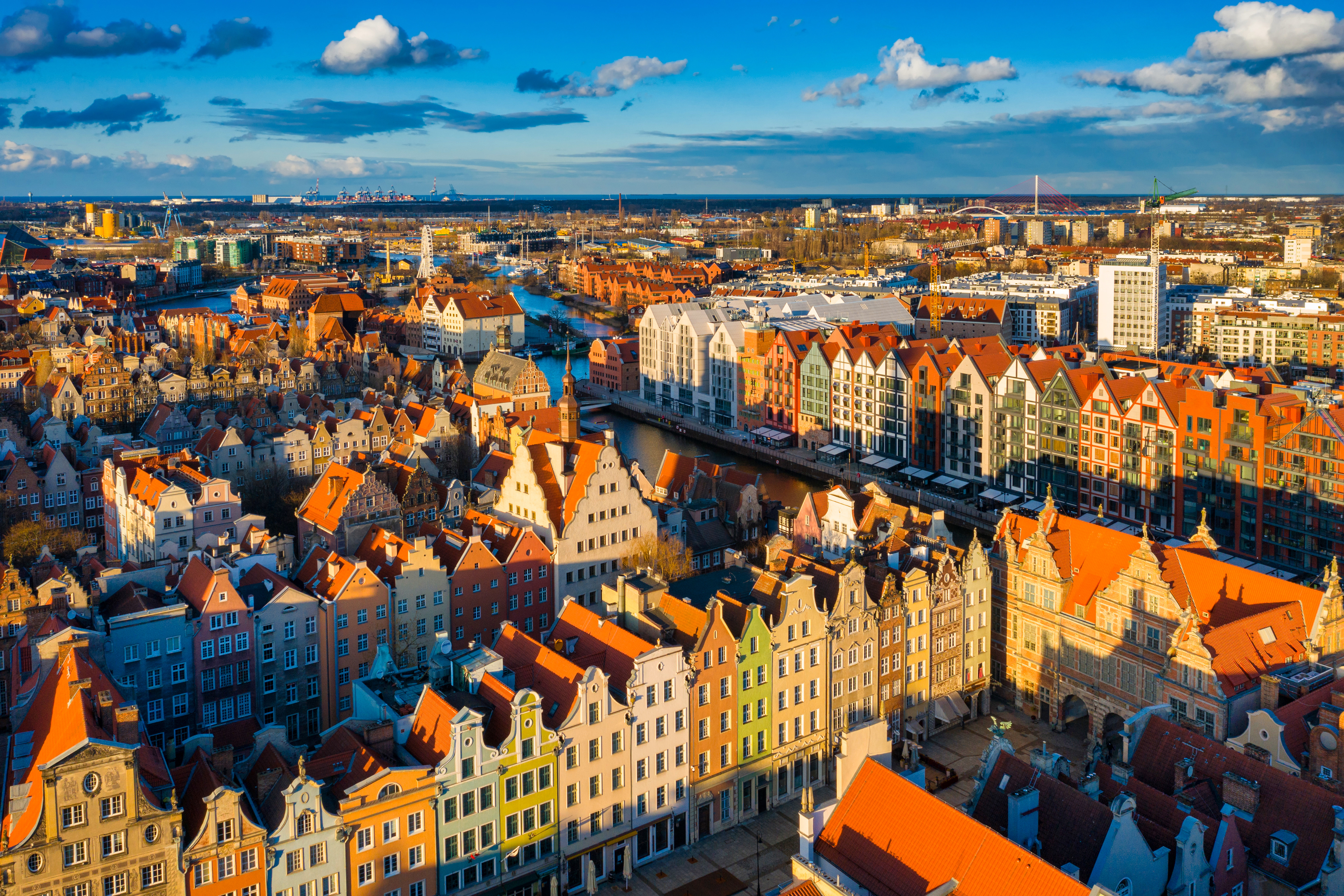 Luftfoto af Gdańsk, Polen, der viser farverige historiske bygninger og røde tage under en klar blå himmel, med bybilledet og havnen i baggrunden