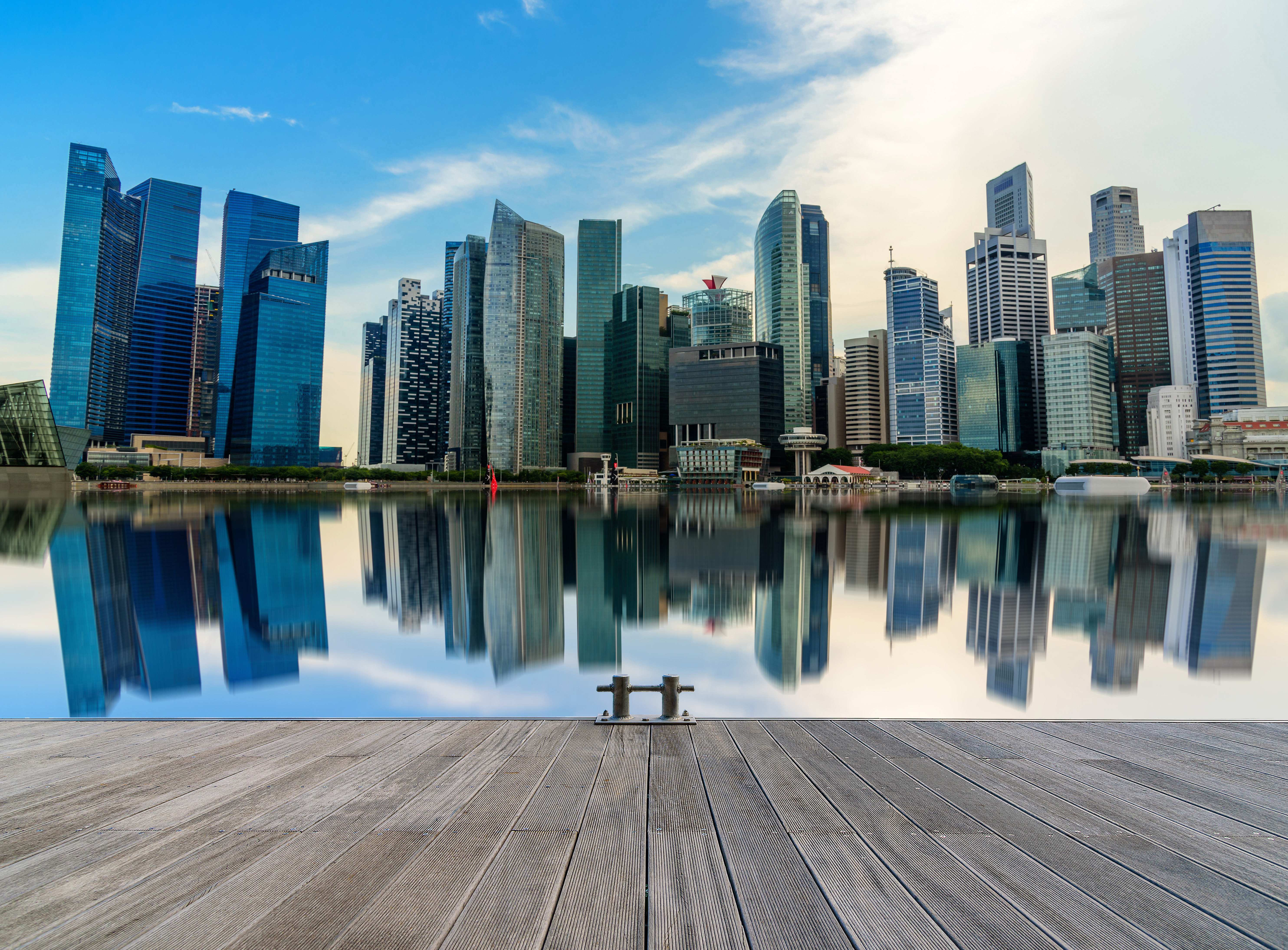 Moderne Singapores skyline med høje skyskrabere, der spejler sig i vandet, set fra en træterrasse på en klar dag
