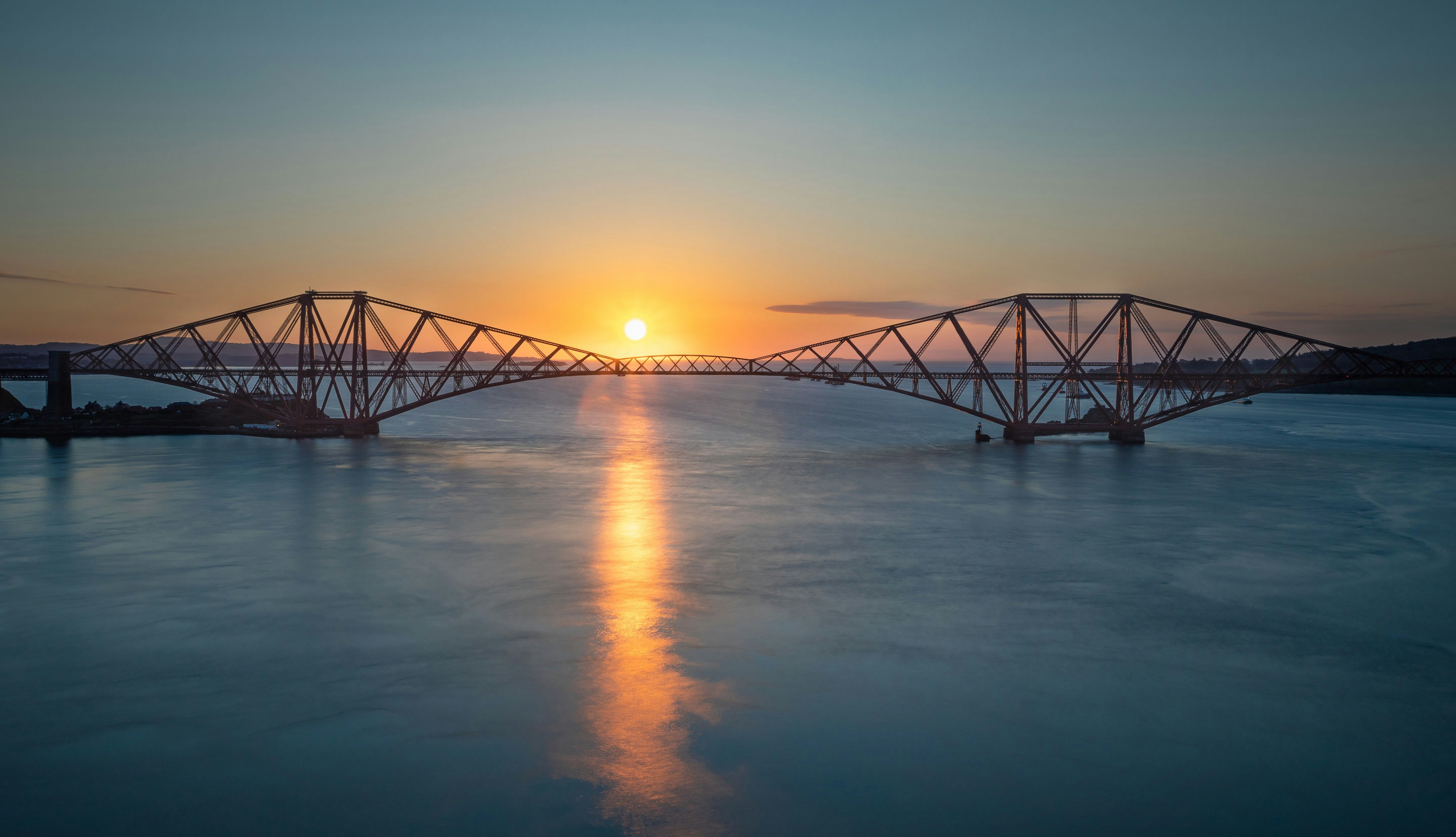 Solnedgang over broen Forth Bridge i Skotland med reflekterende lys på vandet