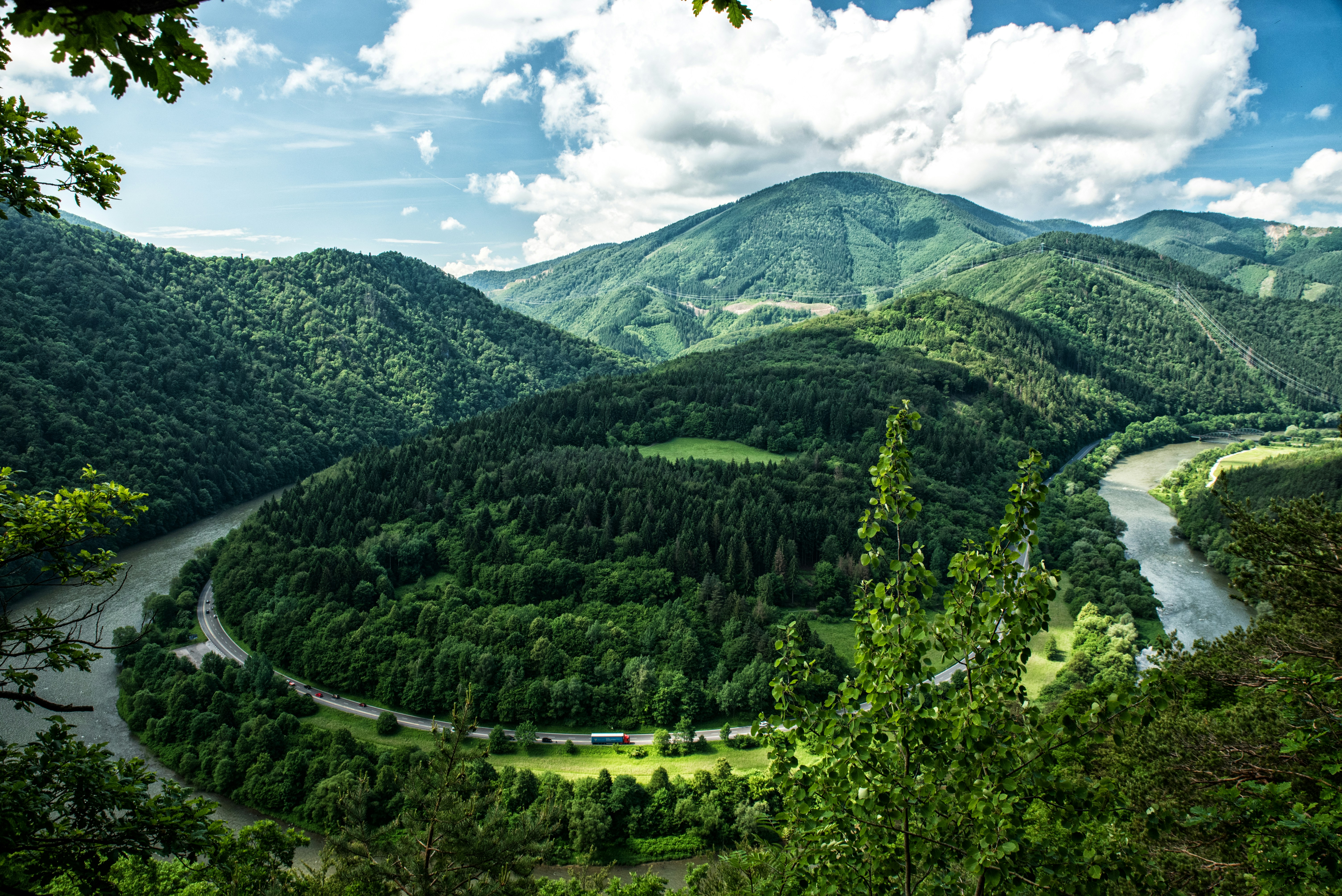 Scenic view of lush green mountains and winding river under a cloudy sky, showcasing natural beauty and landscape diversity