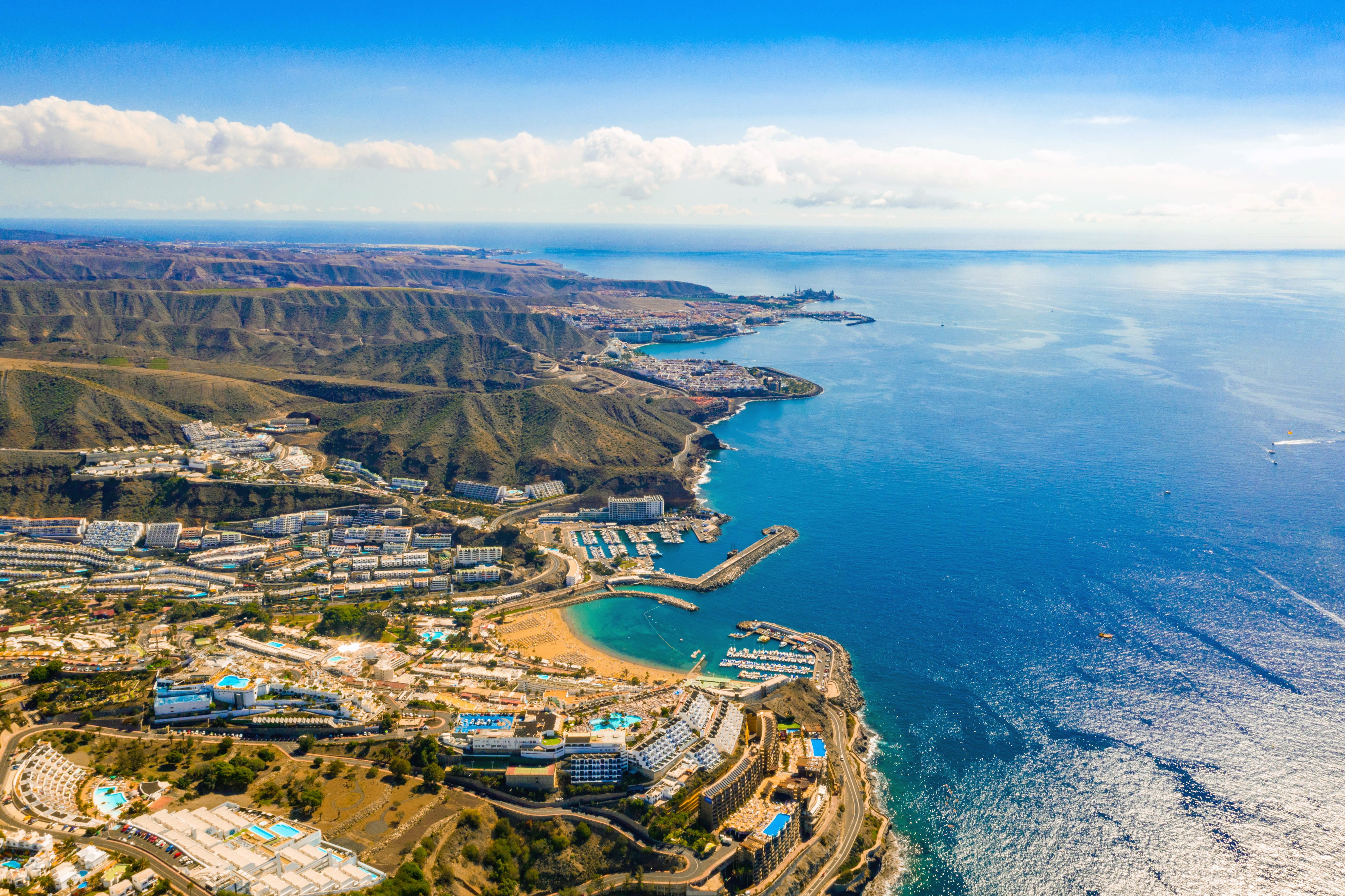 Luftfoto af Gran Canaria kystlinje med azurblåt hav, hvide sandstrande og turistområder omkranset af bjerglandsbyer