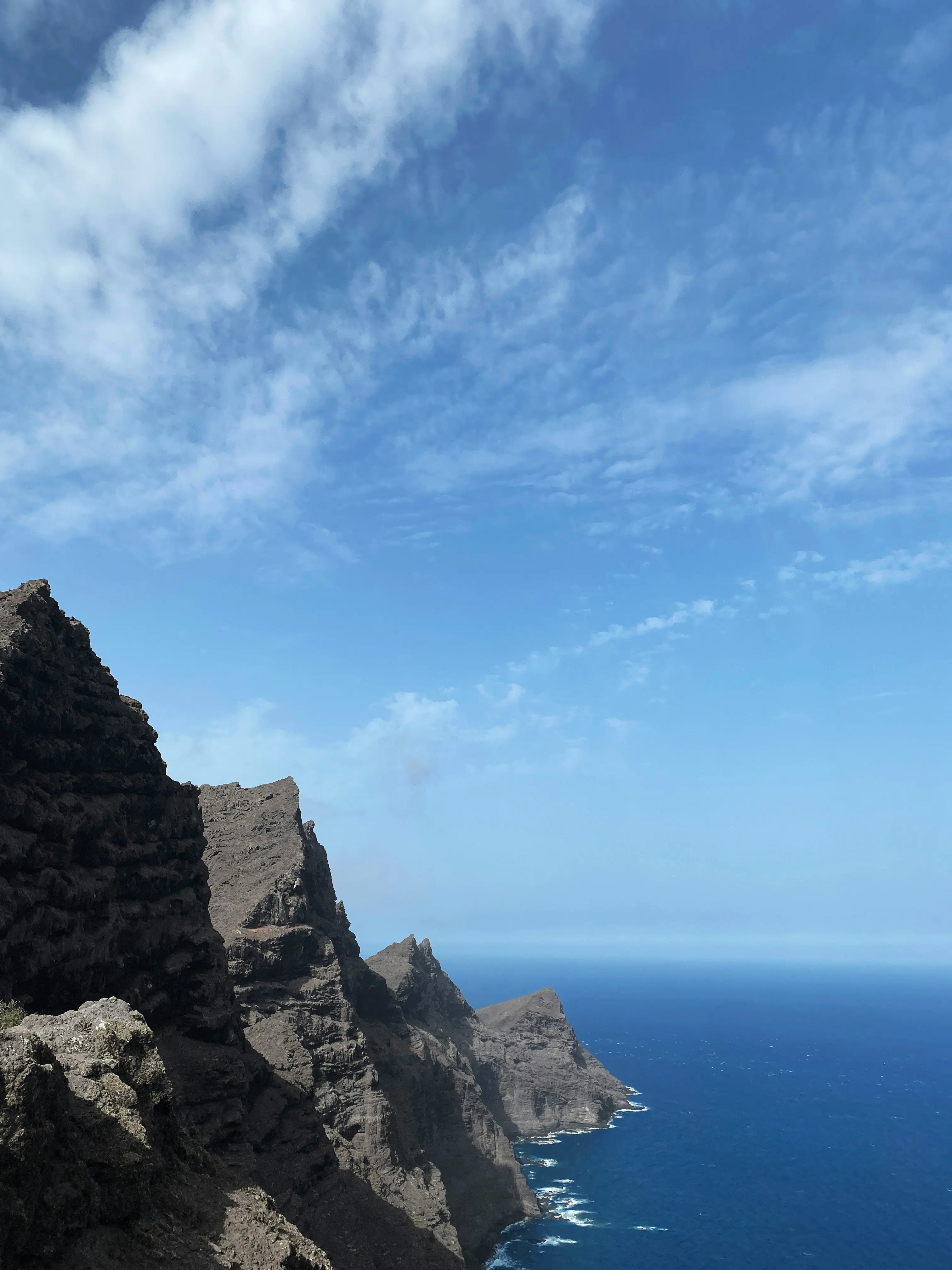 Rocky coastal cliffs meet the deep blue ocean under a partly cloudy sky