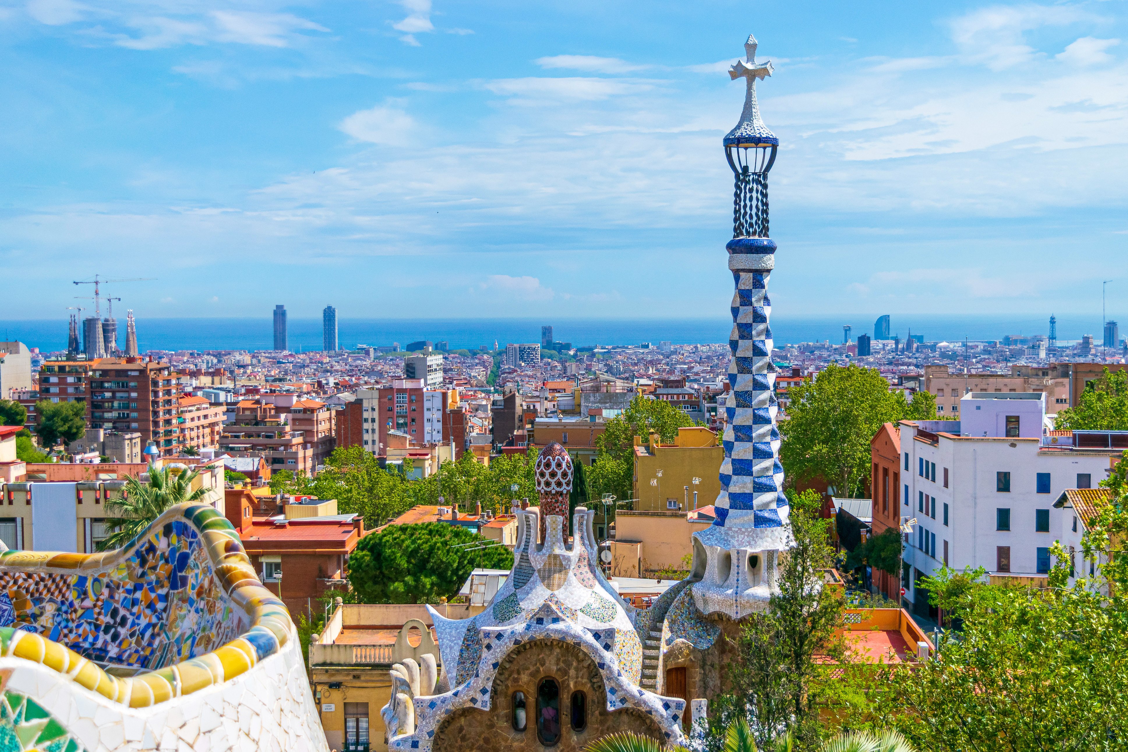 Udsigt over Barcelona fra Park Güell med farverig mosaikarkitektur og byens skyline under en klar blå himmel