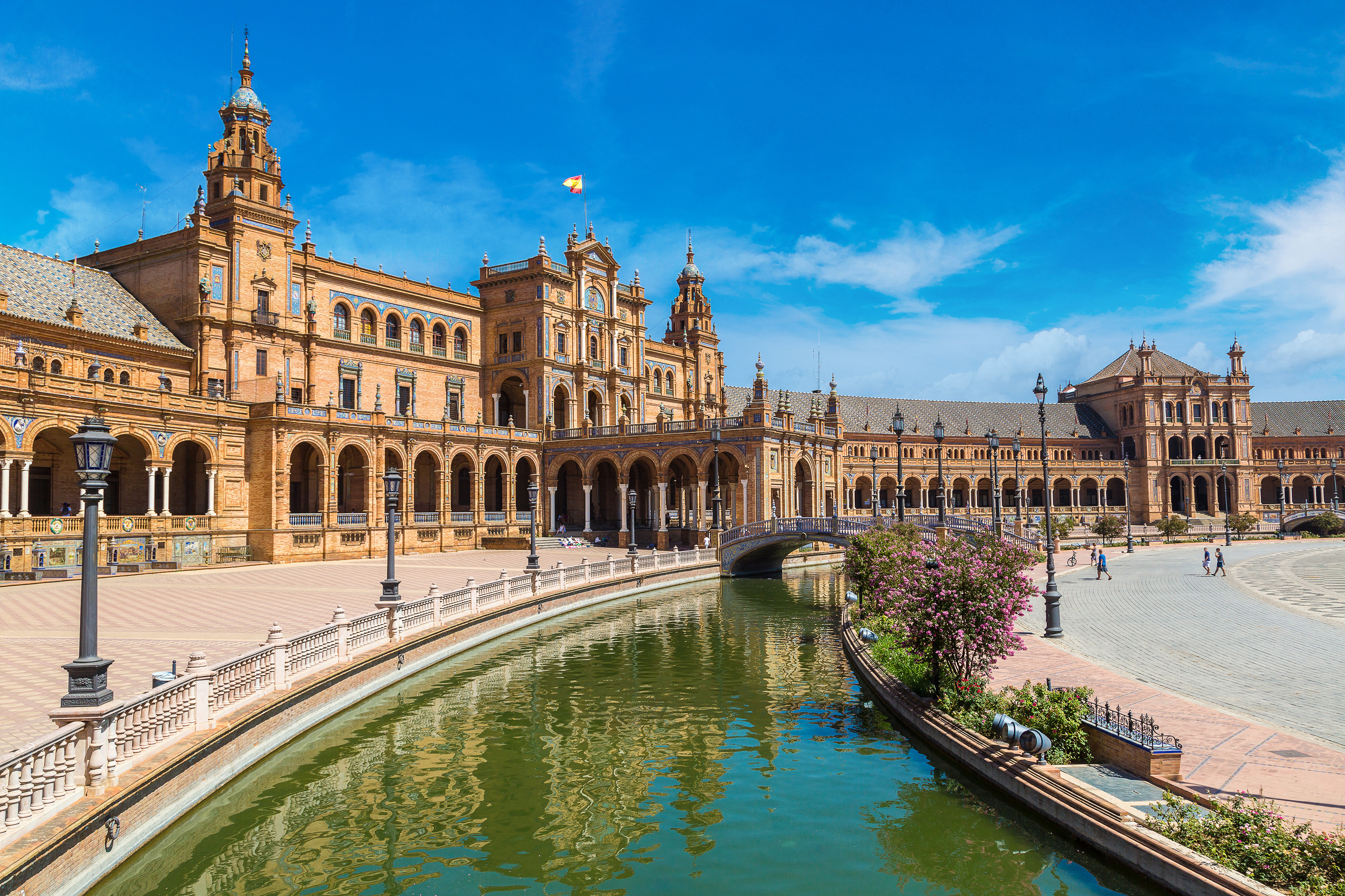 Plaza de España i Sevilla, Spanien, der fremviser sin ikoniske arkitektoniske stil med en omgivende kanal og dekorative broer under en klar blå himmel