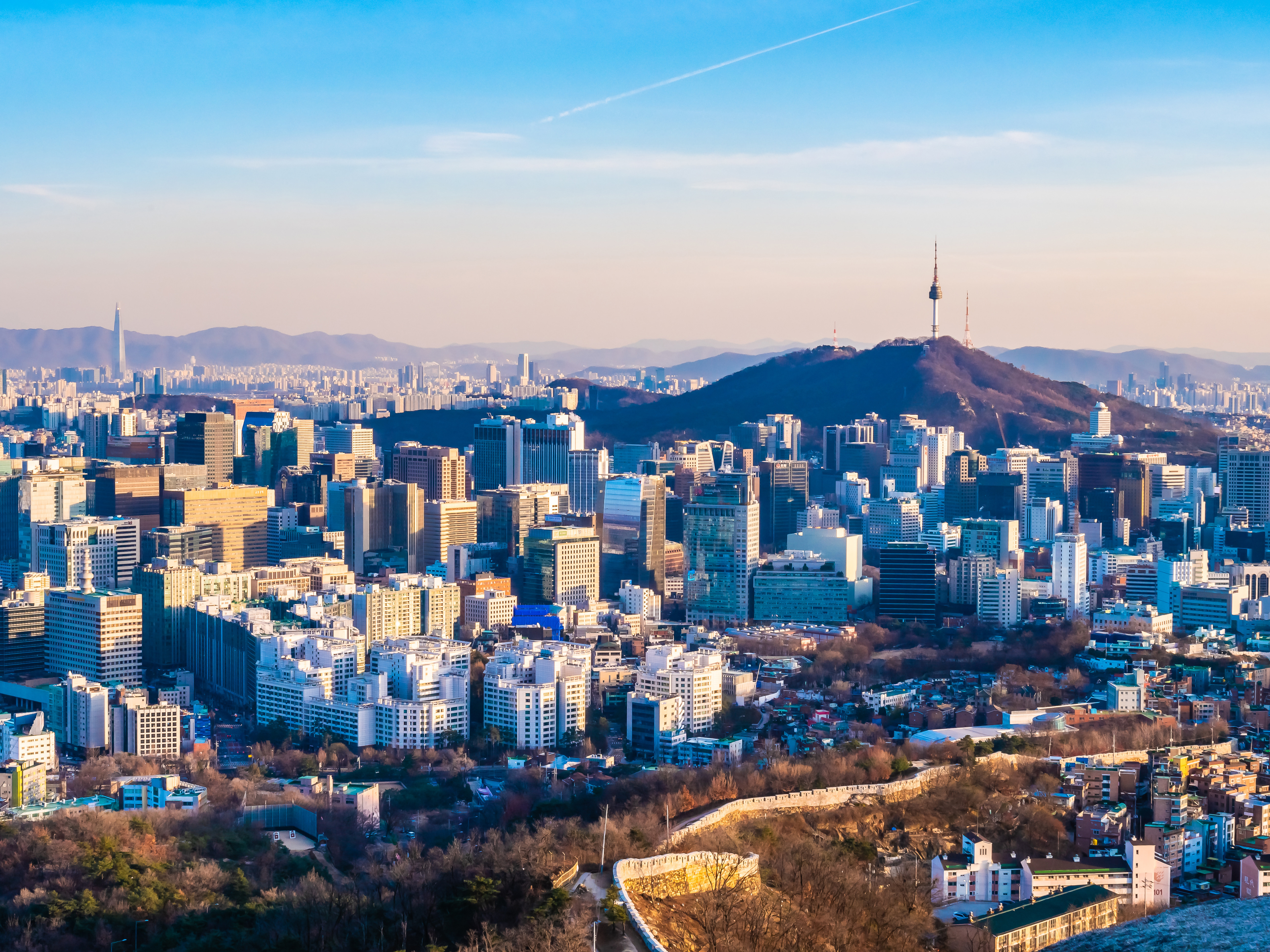 Seoul byens skyline med Namsan-tårnet og bjerge i baggrunden, der viser moderne skyskrabere og bylandskab under en klar blå himmel
