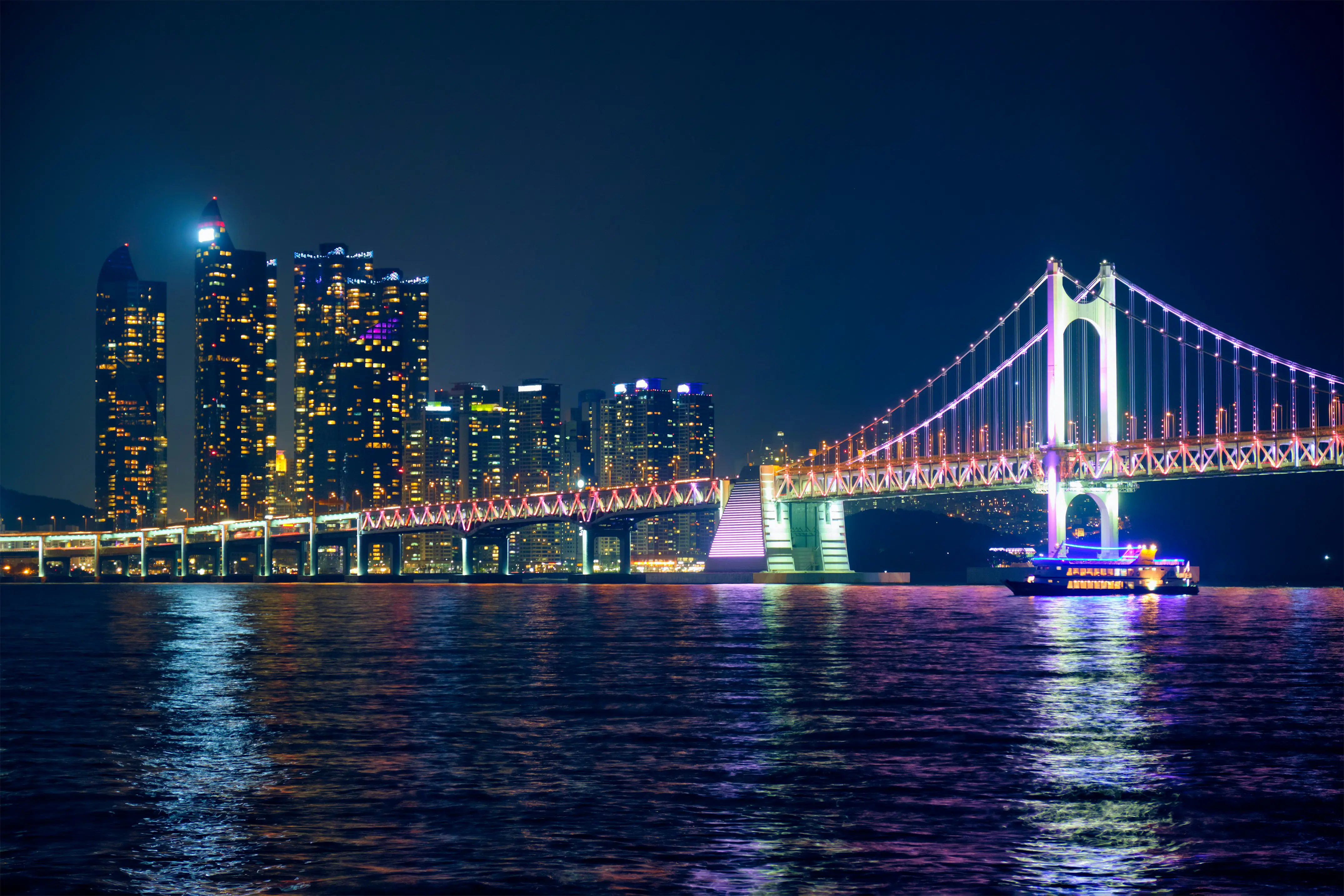 Night view of illuminated Gwangan Bridge and skyscrapers in Busan, South Korea, reflecting on the ocean
