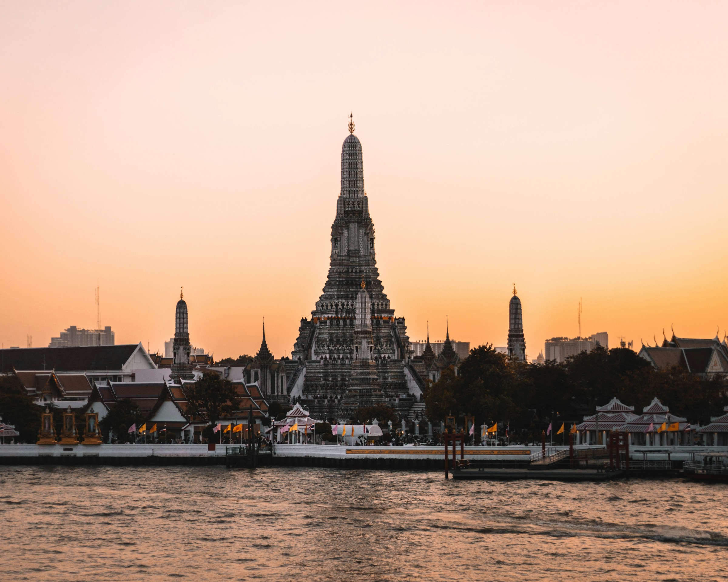 Wat Arun temple silhouetted against a vibrant sunset on the Chao Phraya River in Bangkok, Thailand.