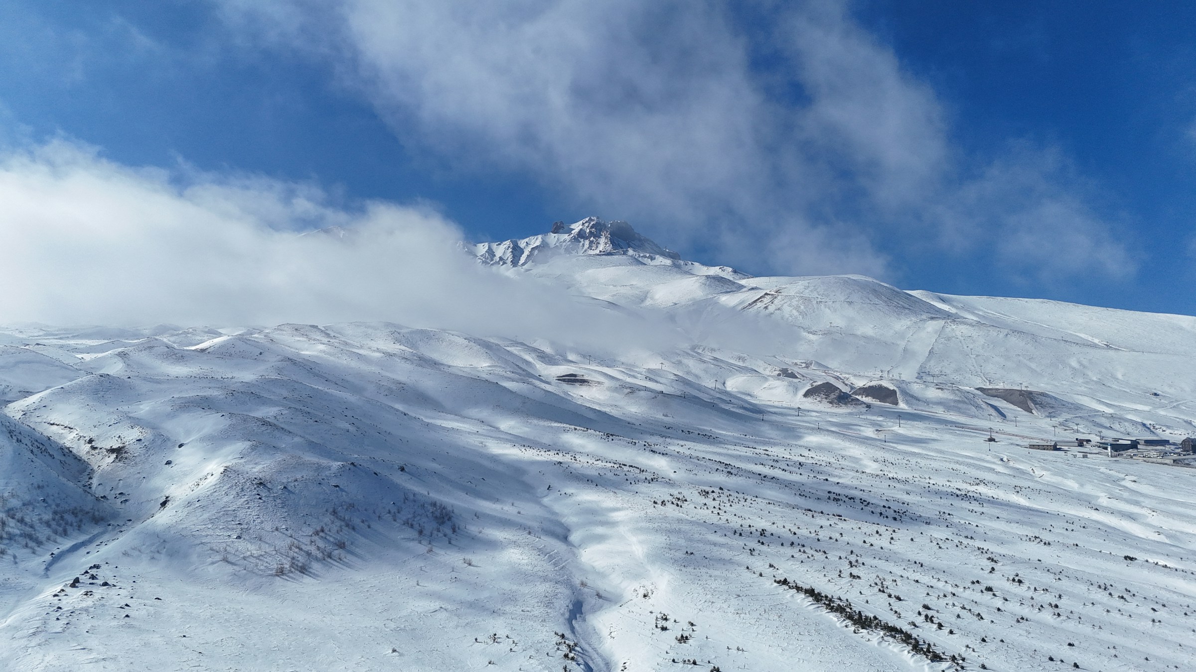Snow-capped mountains under a clear blue sky with clouds at the mountain top of Erciyes, Turkey.