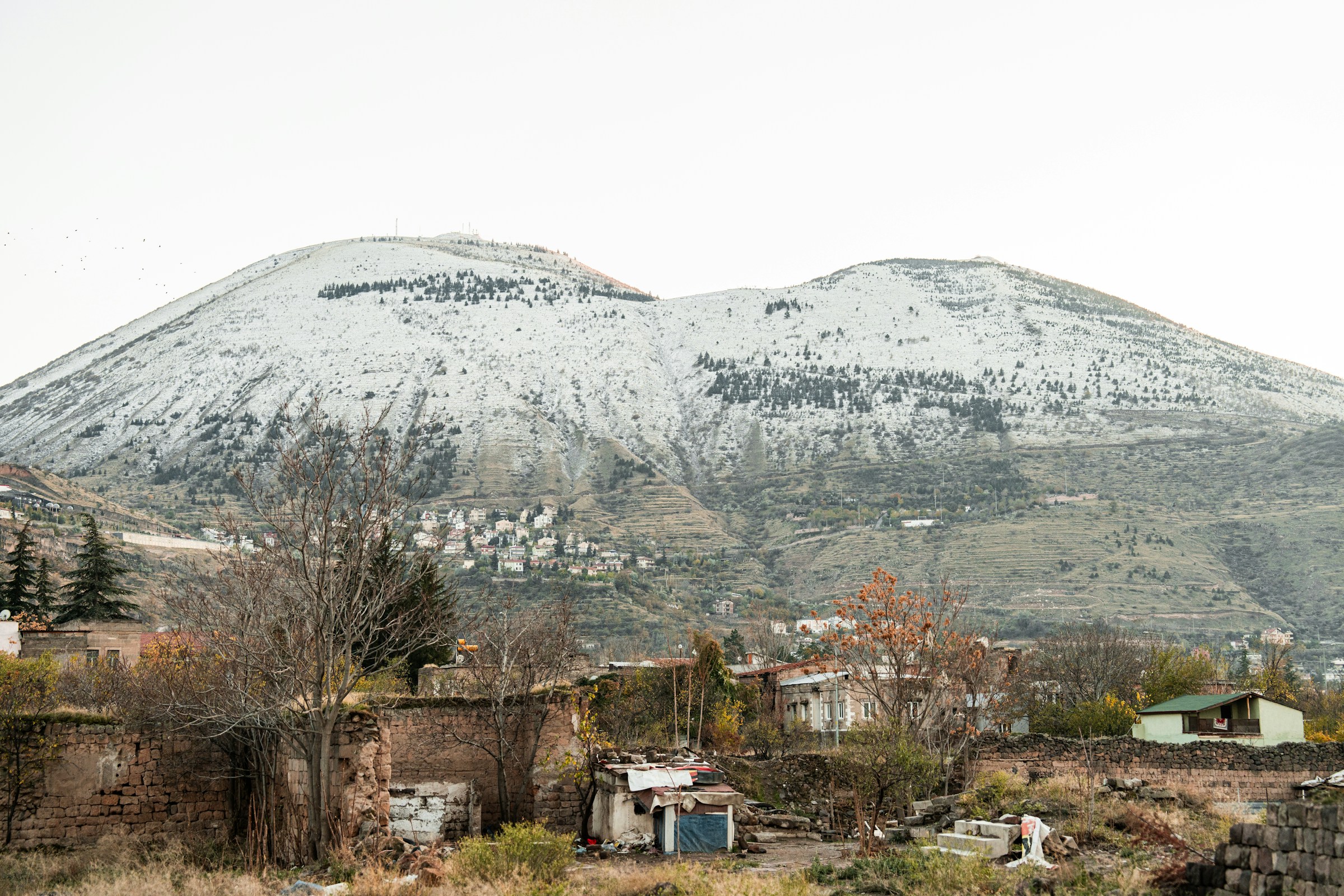 Snow-covered mountain landscape with small houses and trees in the foreground, seen at the base of Mount Erciyes.