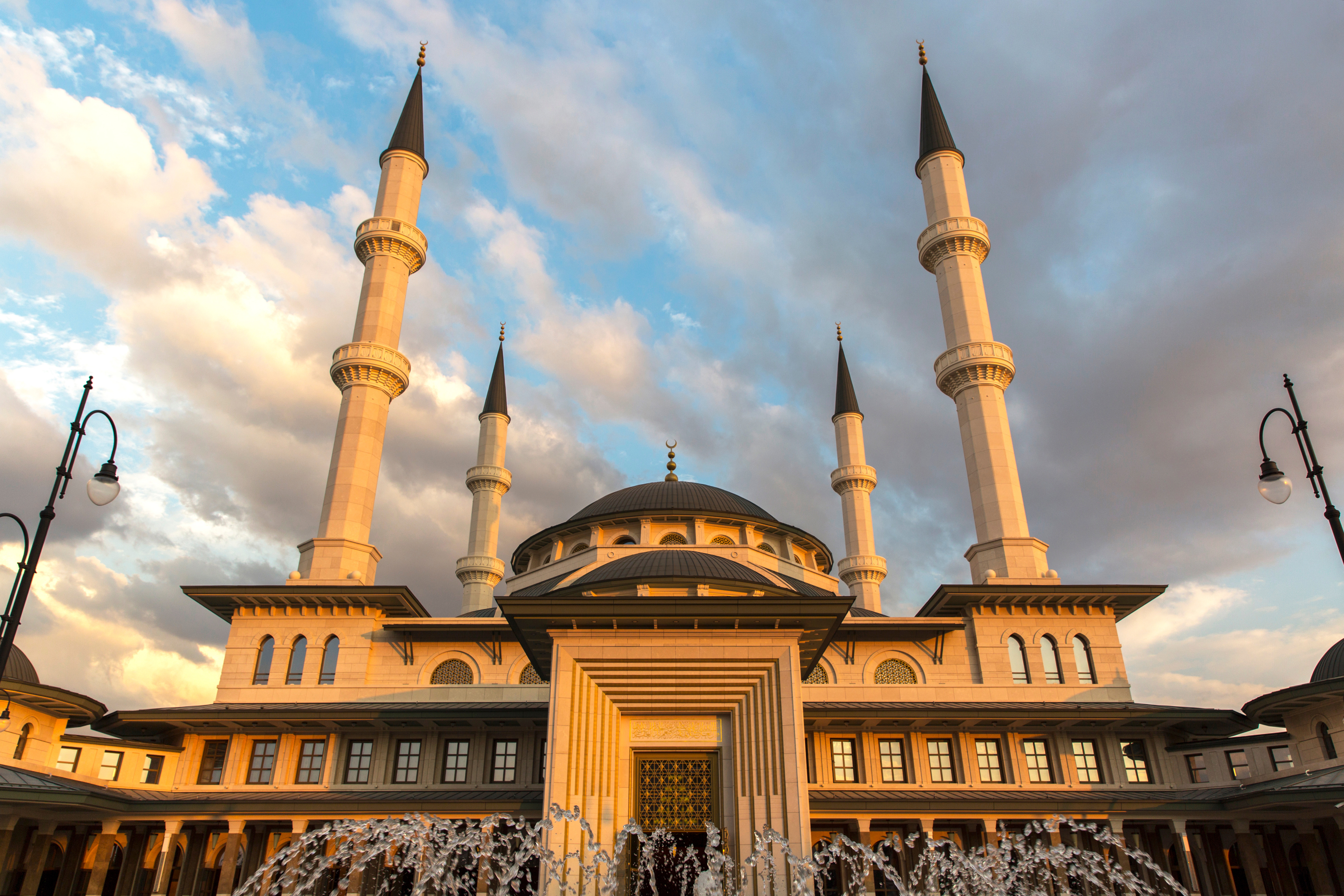 Modern mosque with four tall minarets at sunset, featuring intricate architectural details and a clear sky backdrop