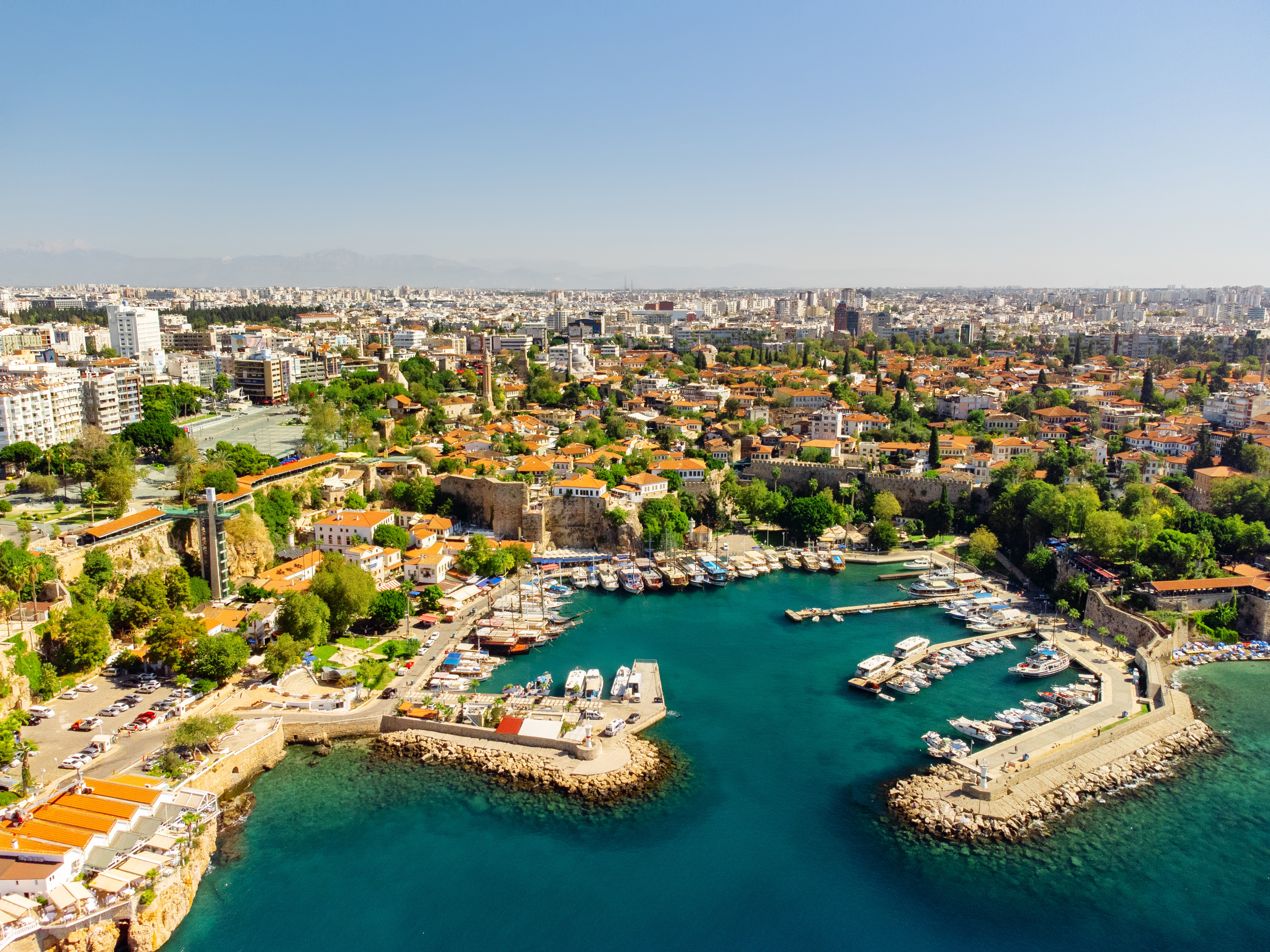 Travel to Antalya - Picturesque harbor with boats, surrounded by historic buildings and lush greenery.