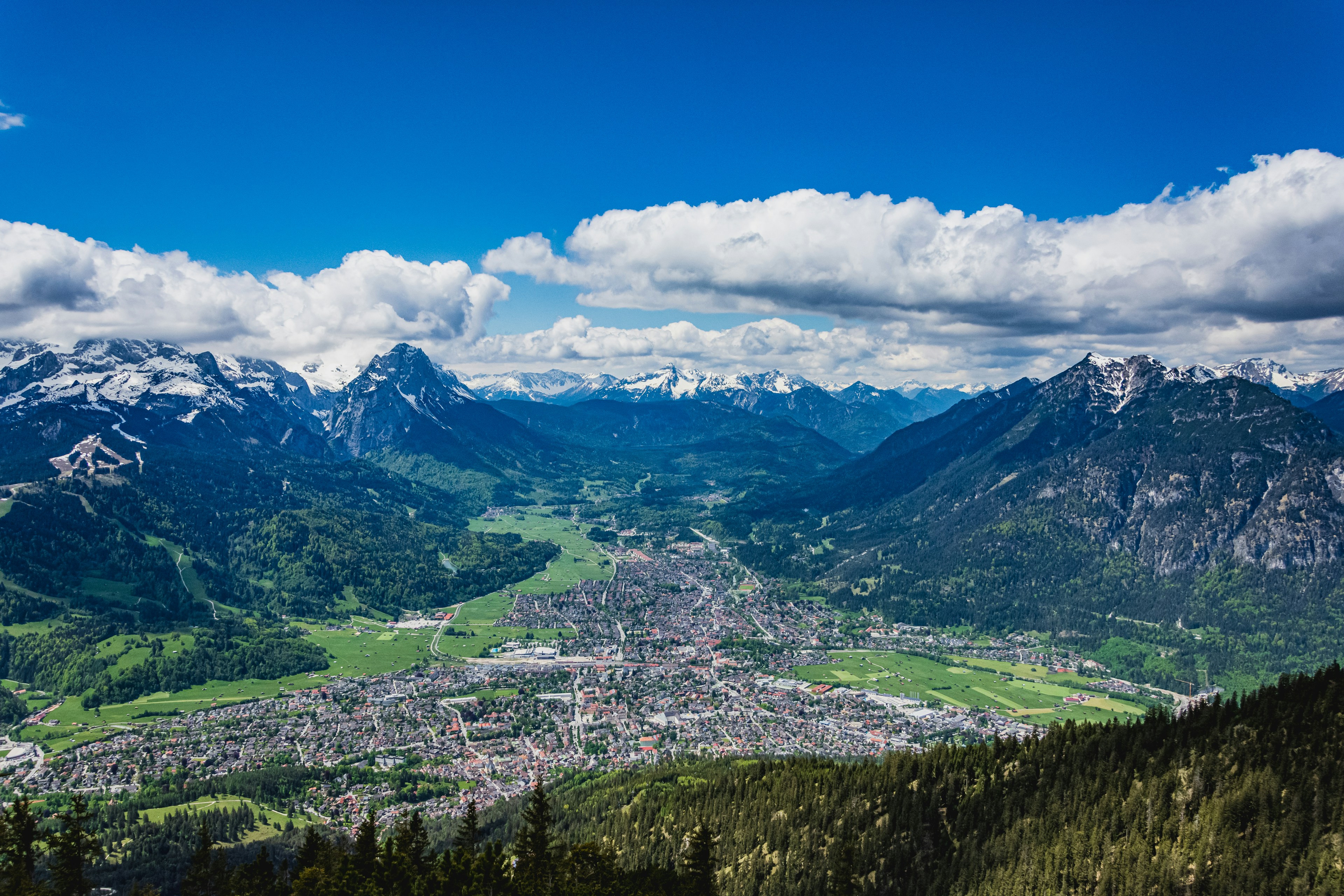 Rejs til Garmisch - Panoramaudsigt over byen mellem skov og mægtige sneklædte bjerge med blå himmel i baggrunden