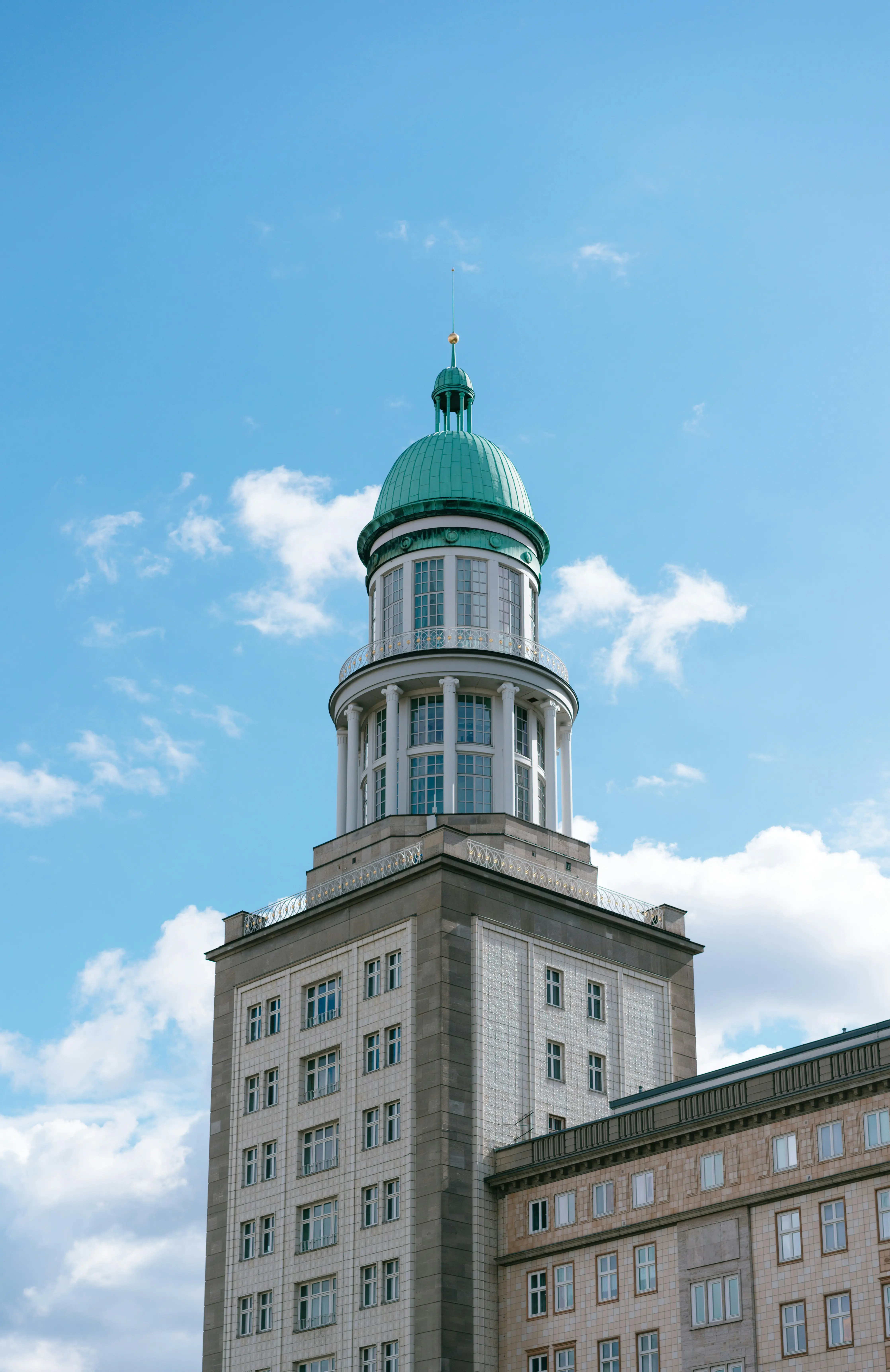 Historisk bygning med grøn kuppel mod blå himmel og skyer, med klassisk arkitektur og adskillige vinduer