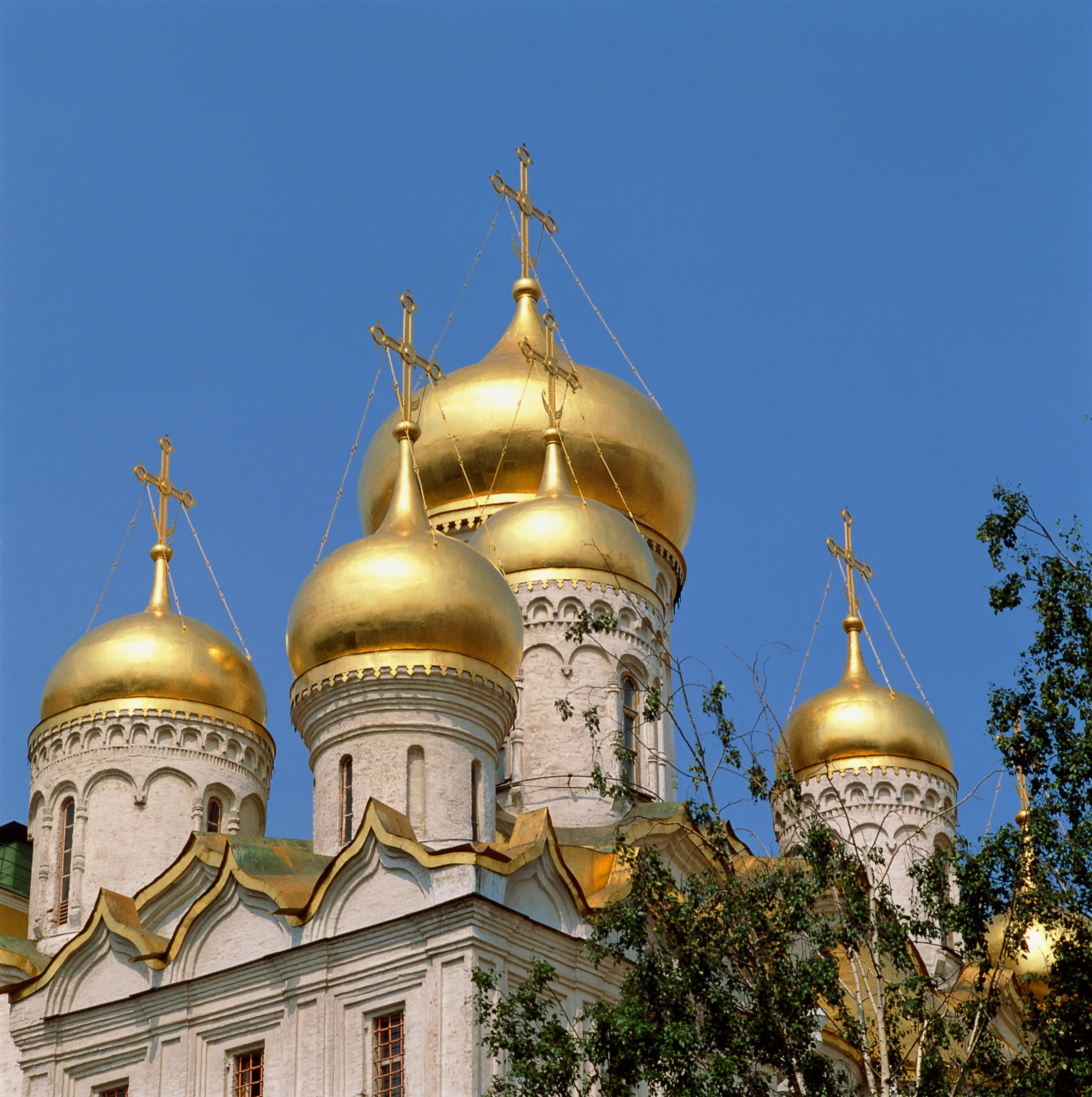 Gyldne kupler på en russisk-ortodoks kirke mod en klar blå himmel, med udsmykkede kors og detaljerede arkitektoniske elementer