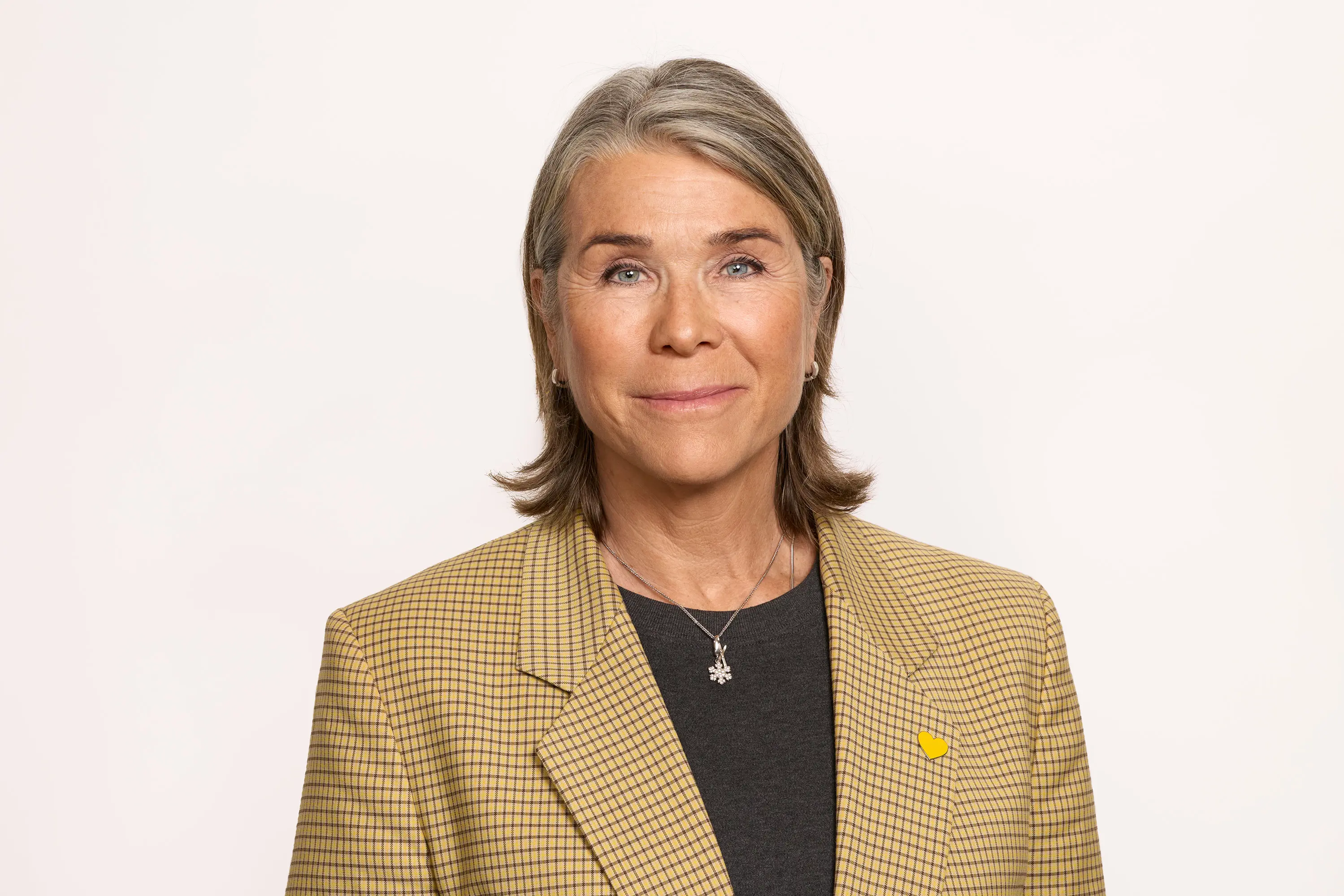 Kvindelig professionel klædt i gul-ternet jakke, smilende, mod en lys baggrund.