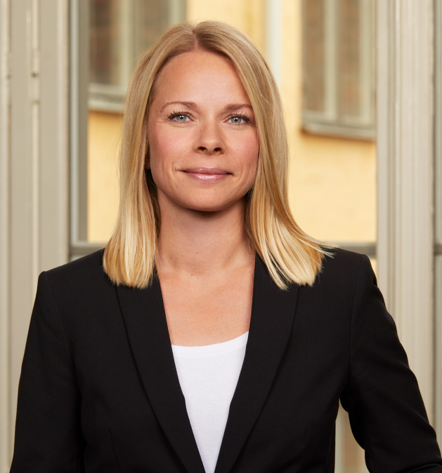 Kvinde i sort blazer med langt blondt hår står foran et vindue.