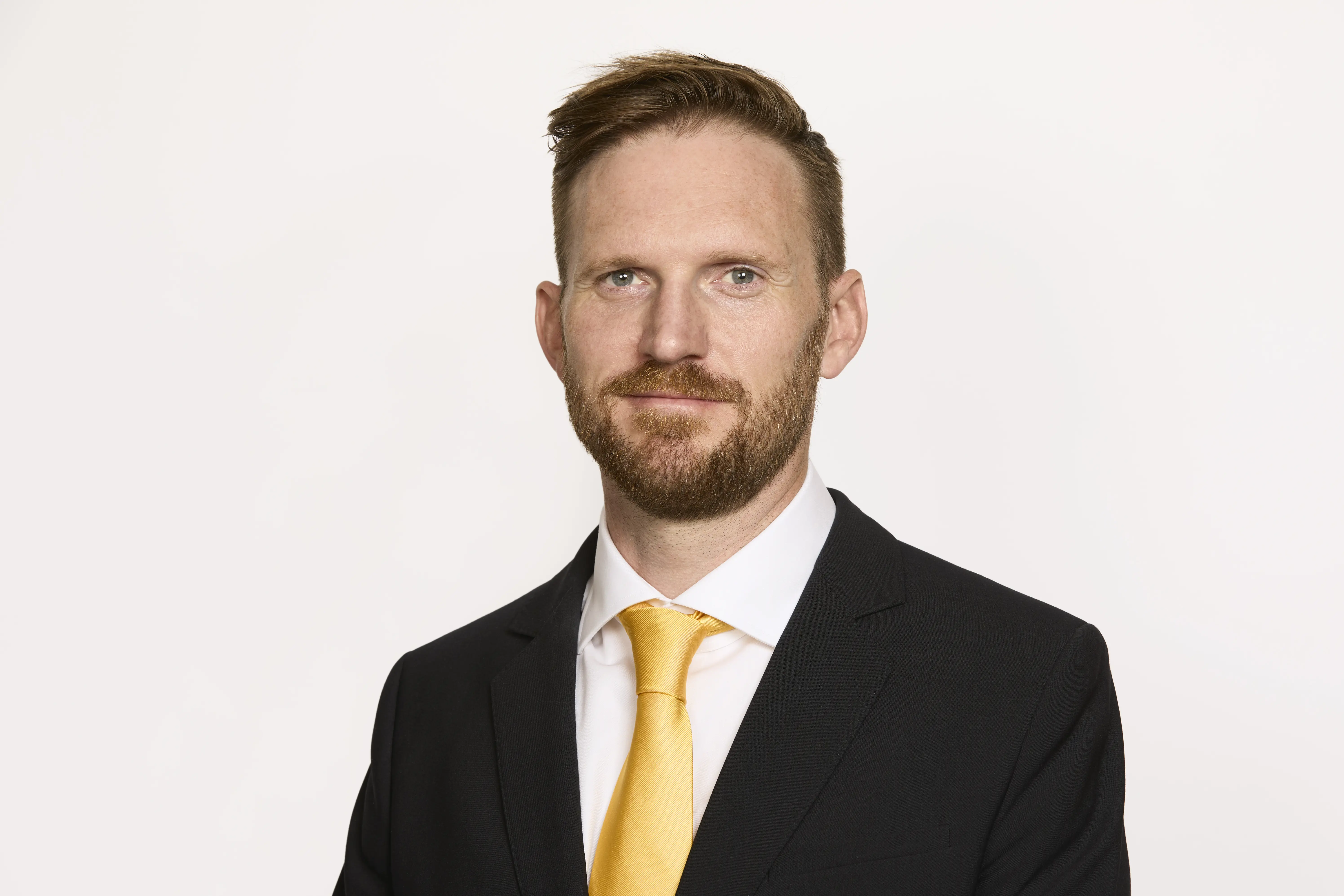 Mand i jakkesæt med gul slips ser formelt ud, står foran en lys baggrund.