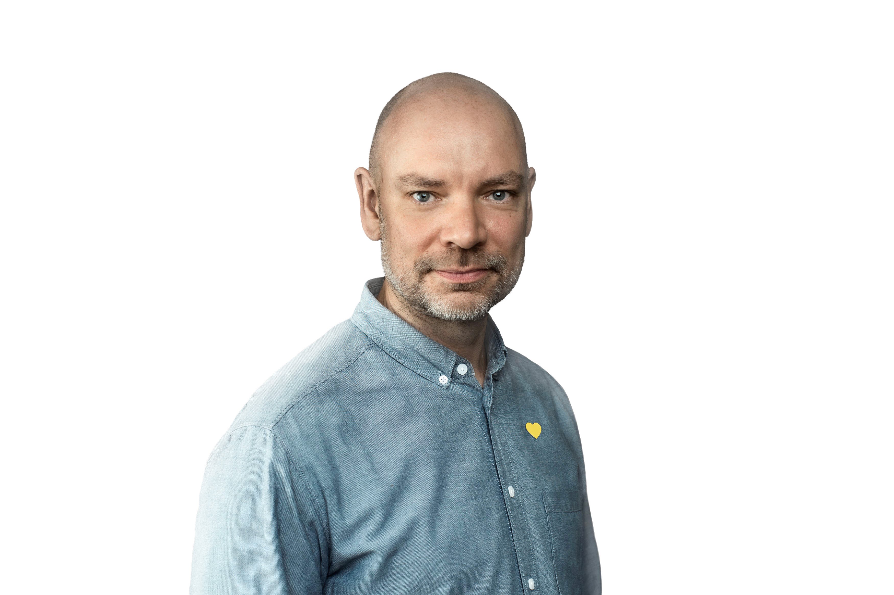 Mand iført en lyseblå skjorte med gul hjertelogo på brystet, står foran en hvid baggrund.