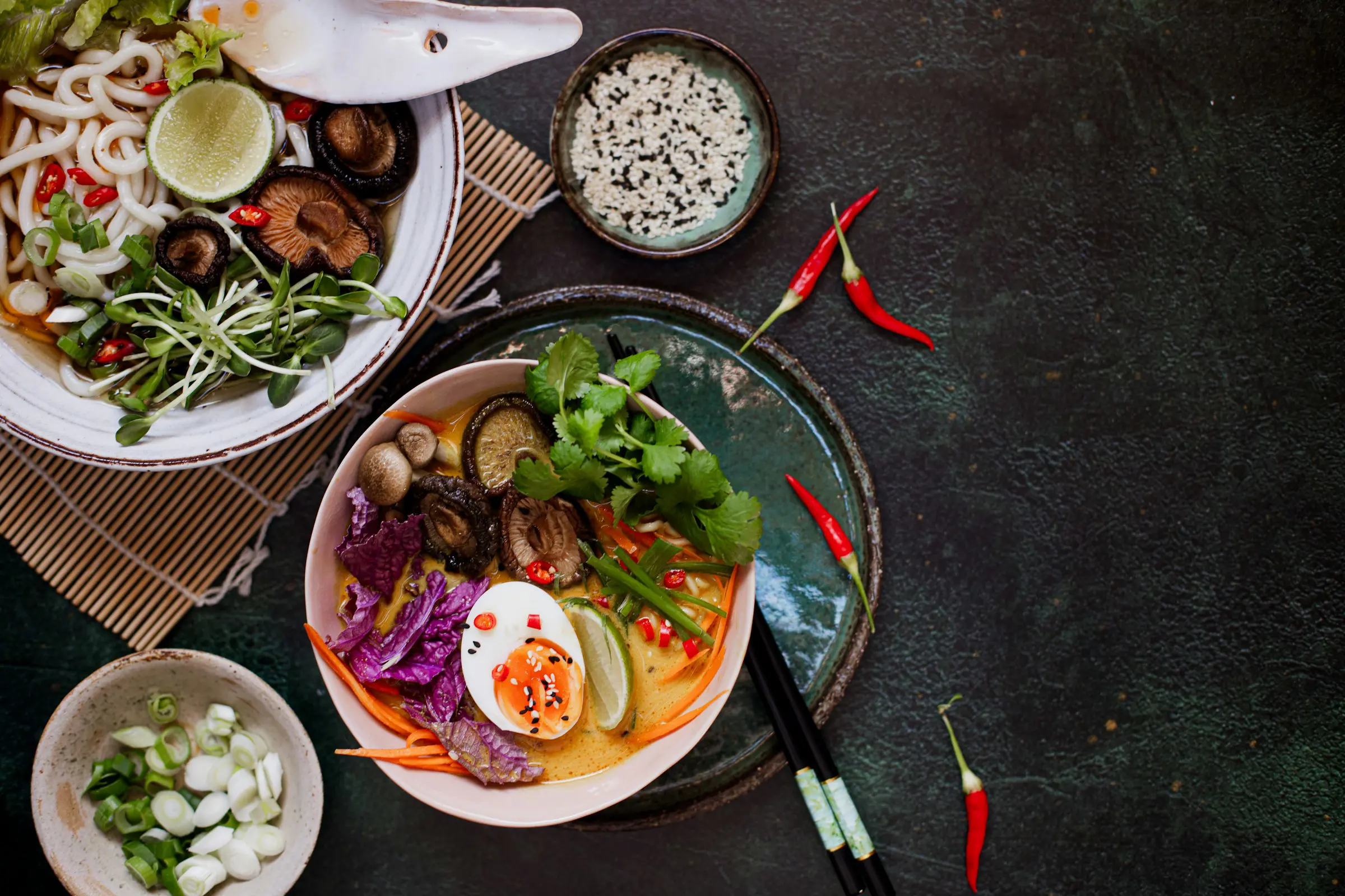 Asiatiske nudelskåle med grøntsager, lime, champignon og æg på mørk baggrund, dekoreret med koriander og chilipeber.