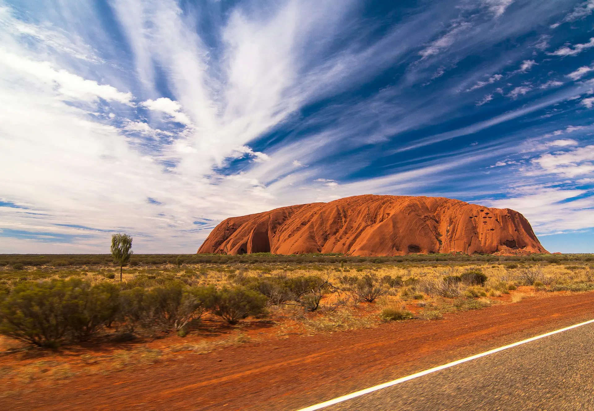 Uluru klippeformation i Australiens ørkenlandskab under en blå himmel med dramatiske skyer